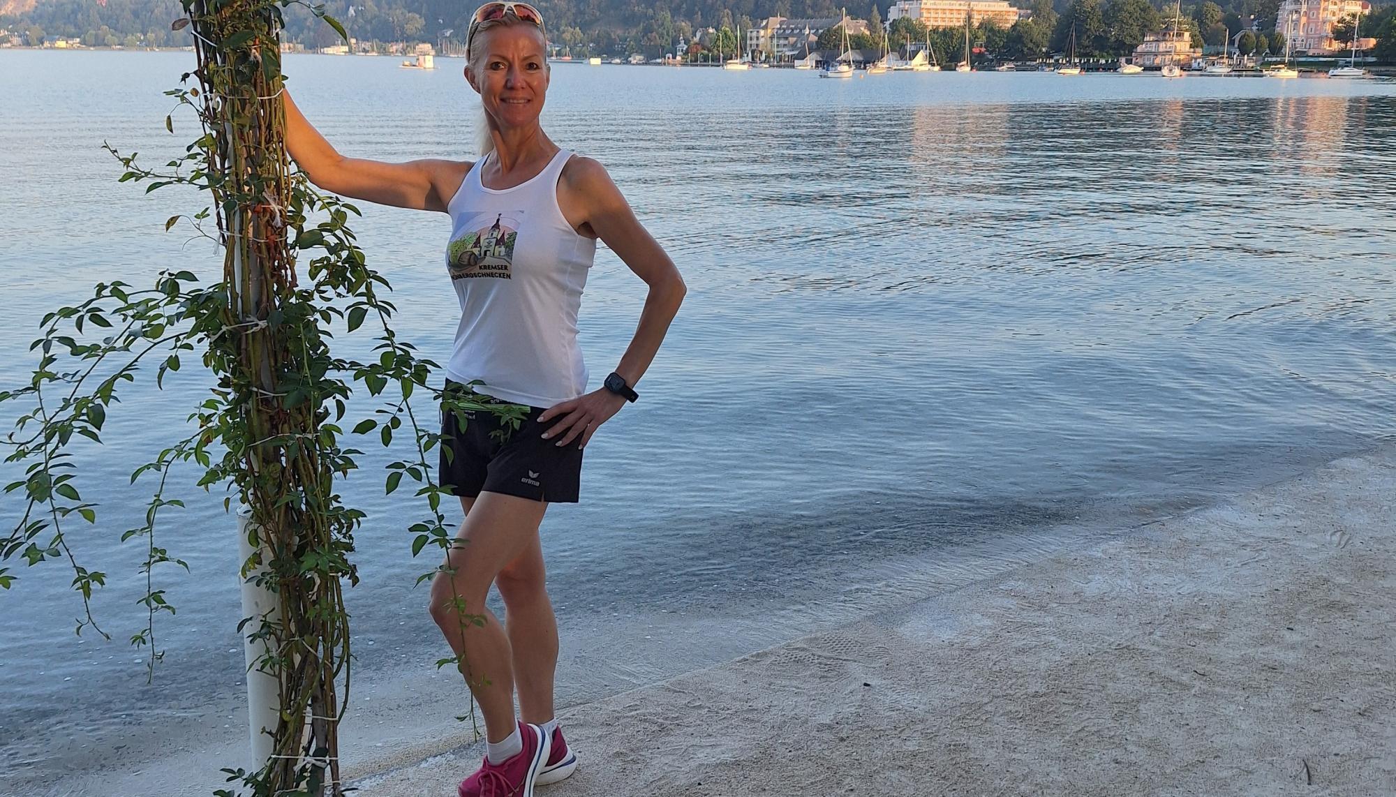 Eine Frau steht am Ufer eines Sees, im Hintergrund sind Gebäude und Boote zu sehen.