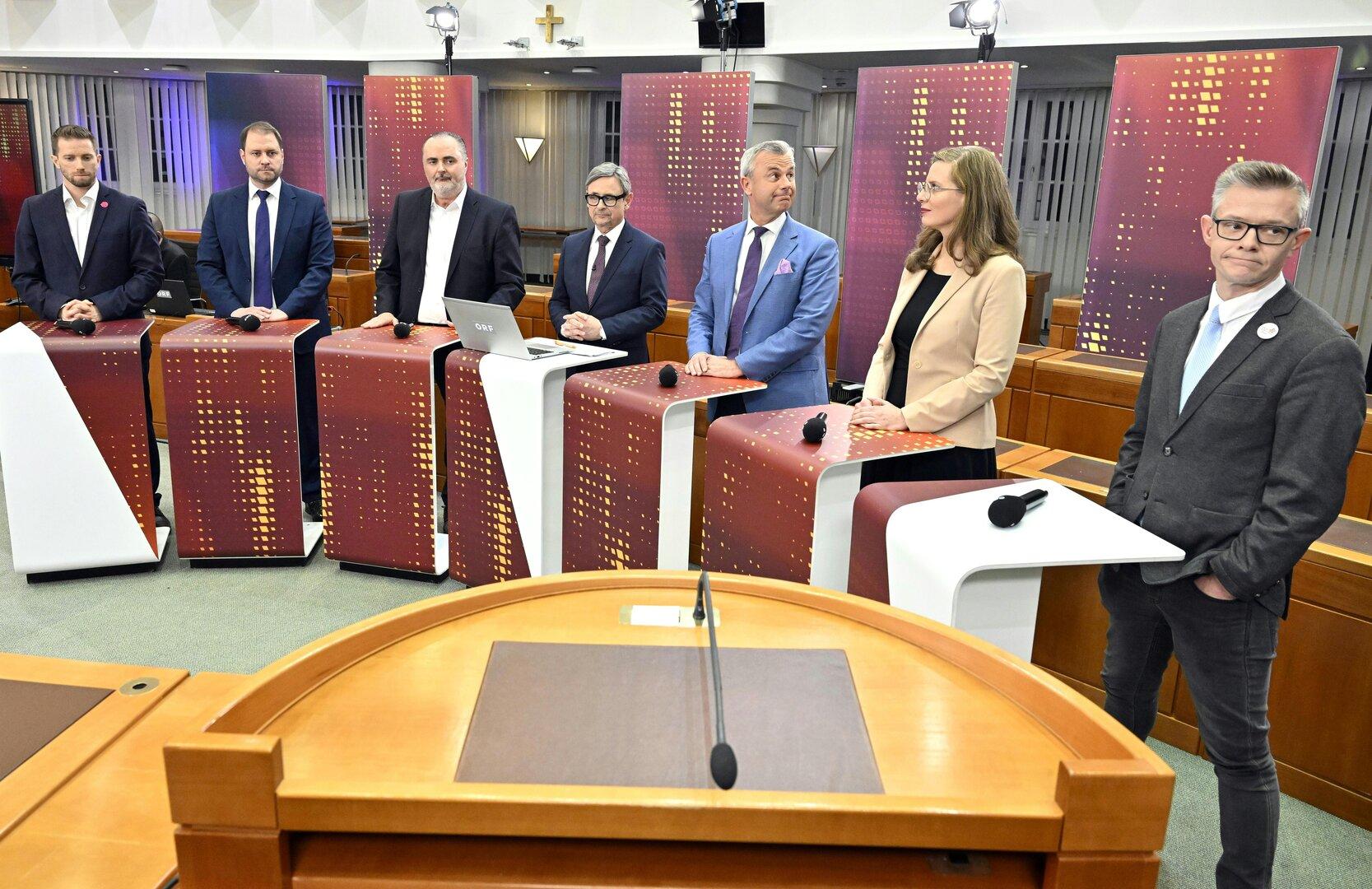 Mehrere Personen stehen hinter Rednerpulten in einem Fernsehstudio.
