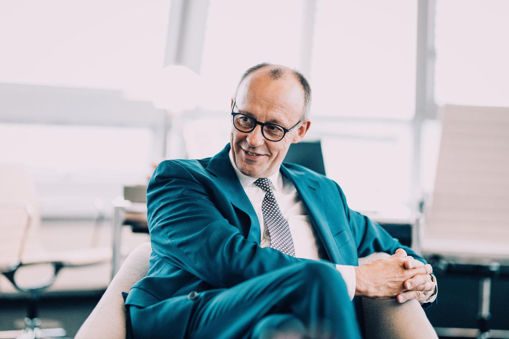 Friedrich Merz sitzt in einem Sessel und lächelt.