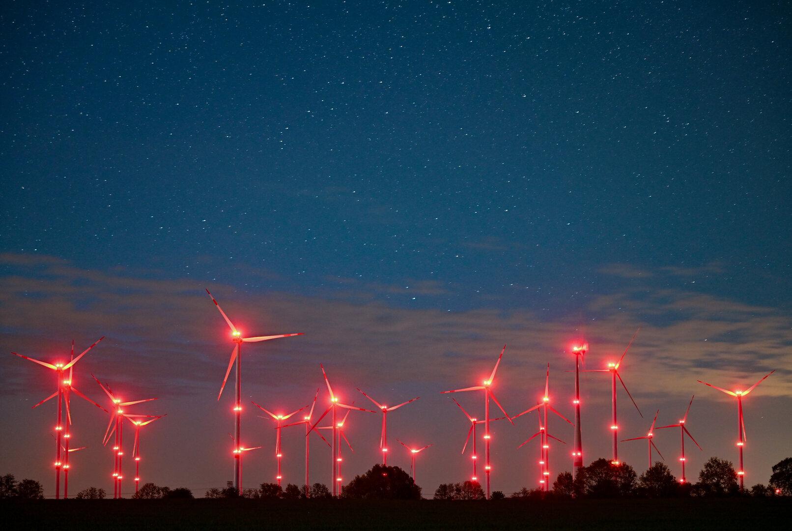 Windräder mit roter Beleuchtung unter einem Sternenhimmel.