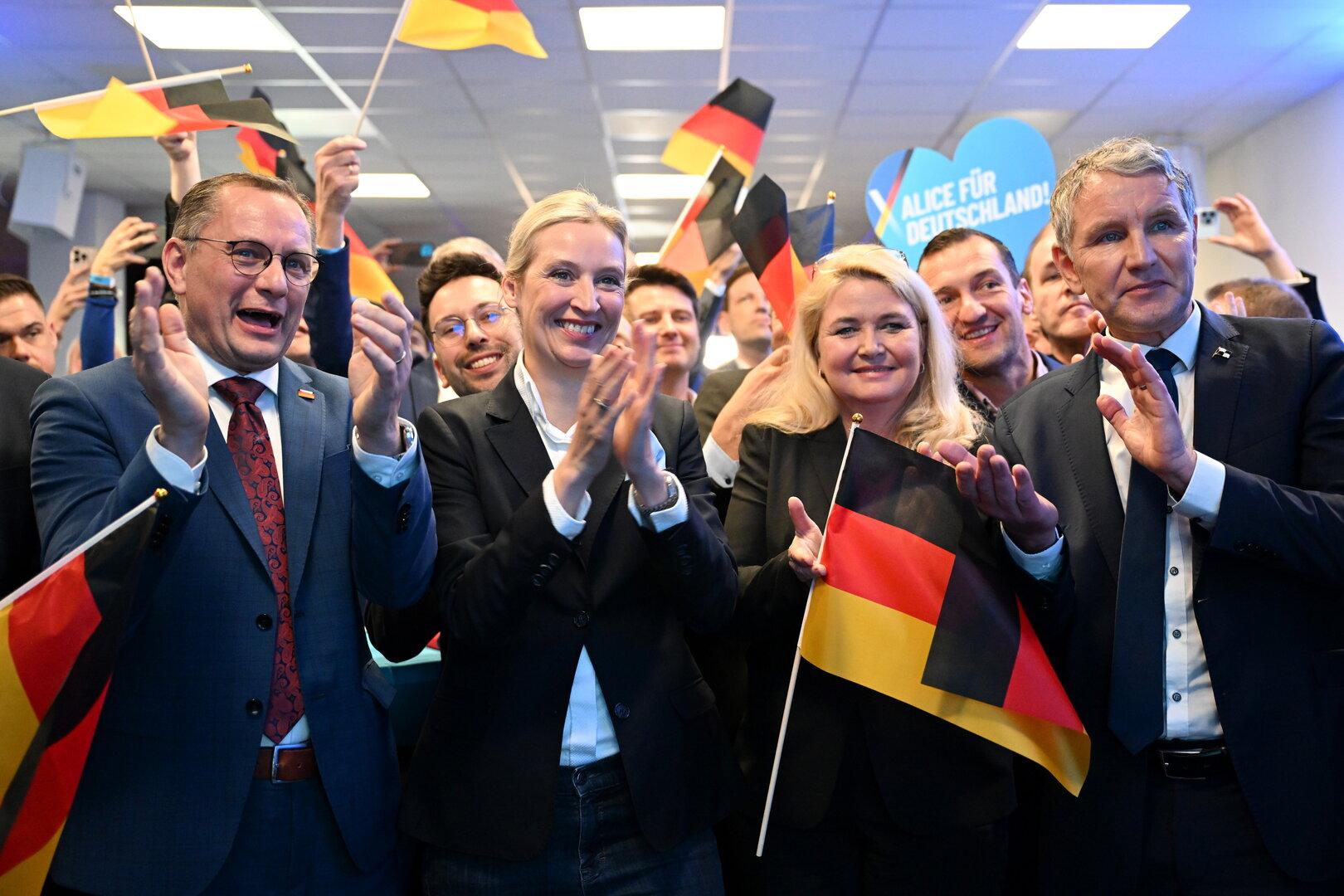 Mehrere Personen, darunter Politiker, applaudieren und schwenken Deutschlandfahnen.