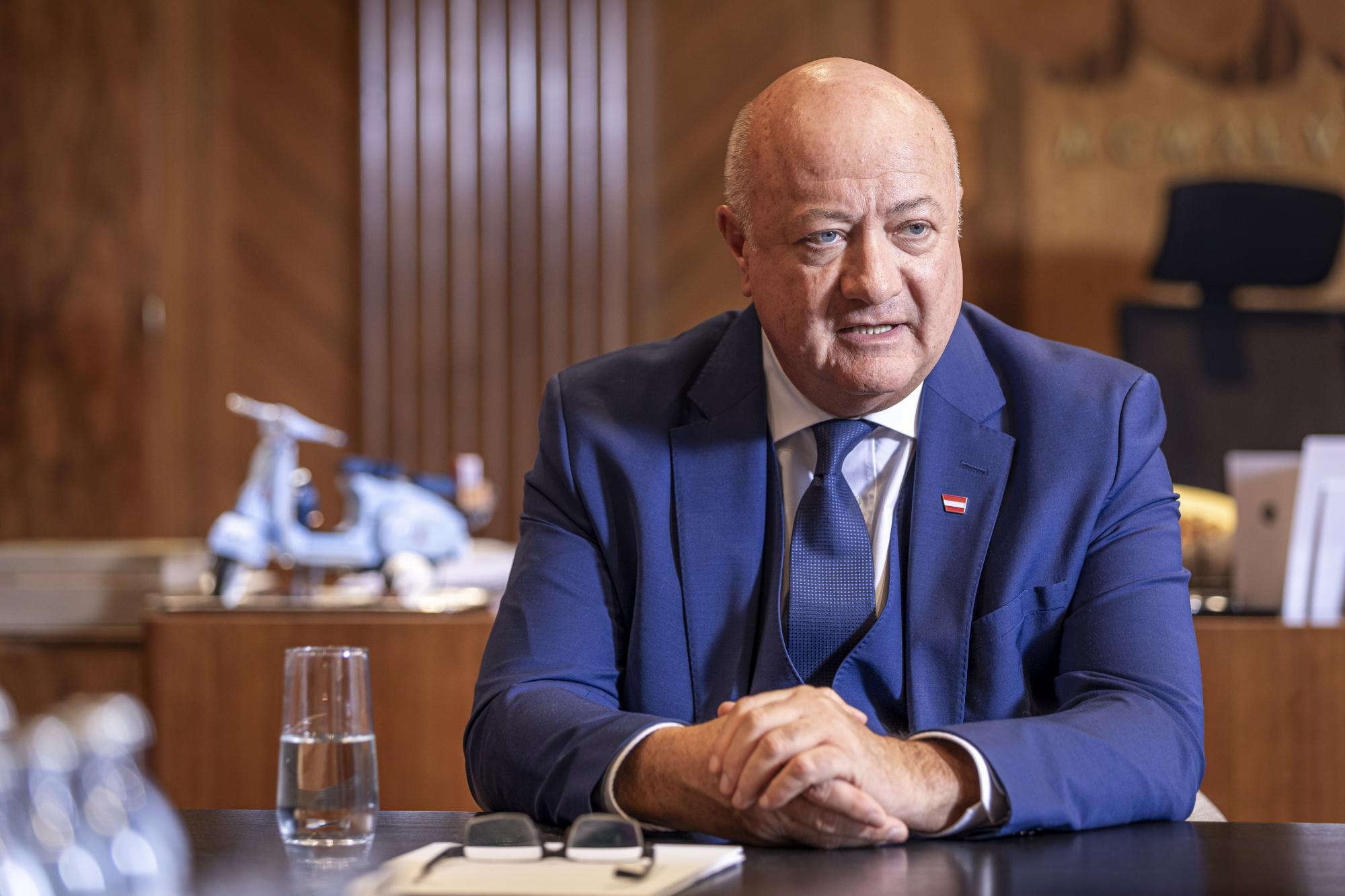 Christian Stocker sitzt an einem Tisch mit einer kleinen Vespa im Hintergrund.