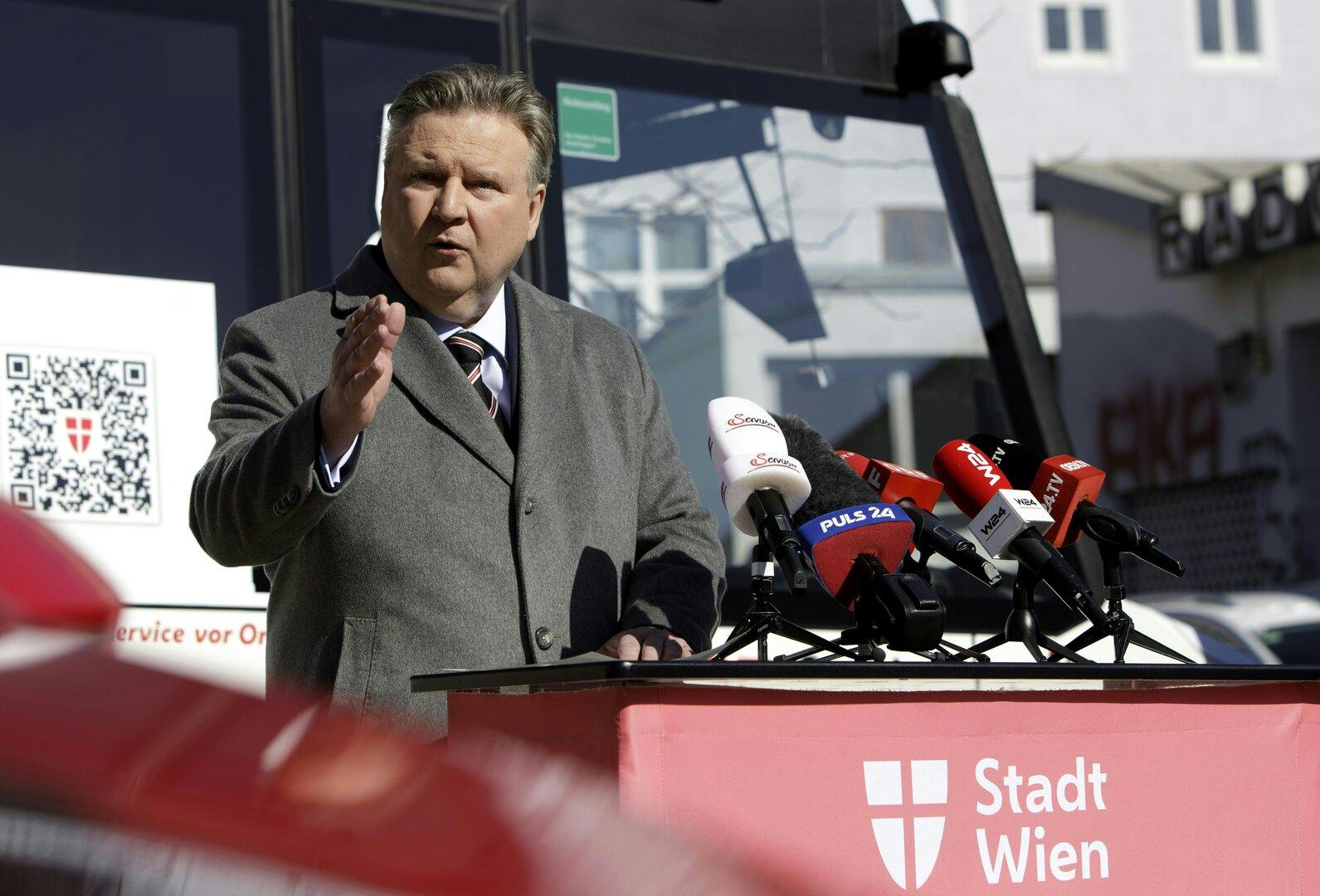 Ein Mann spricht vor Mikrofonen mit Logos verschiedener Fernsehsender und „Stadt Wien“.