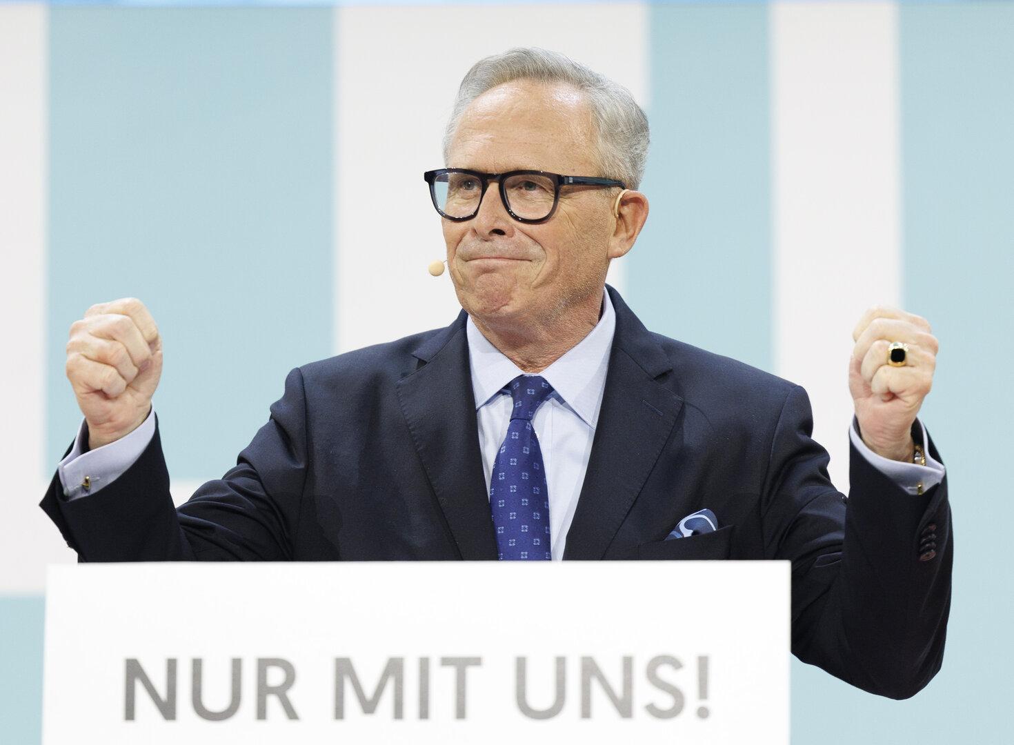 Ein Mann in Anzug steht hinter einem Rednerpult mit der Aufschrift „NUR MIT UNS!“.