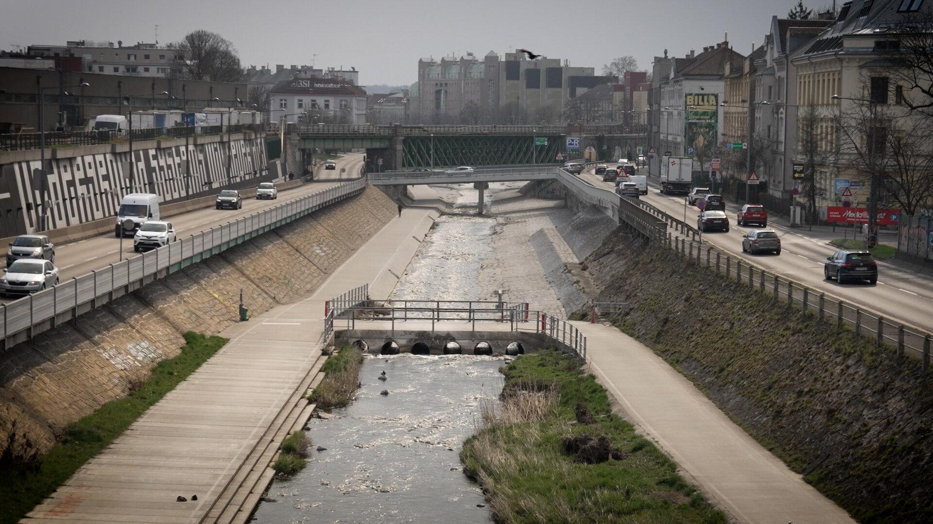 Der Wienfluss fließt kanalisiert durch Wien, flankiert von Straßen und Gehwegen.