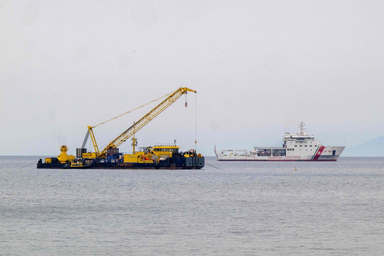 Ein gelber Schwimmkran und ein Schiff der italienischen Küstenwache auf dem Meer.