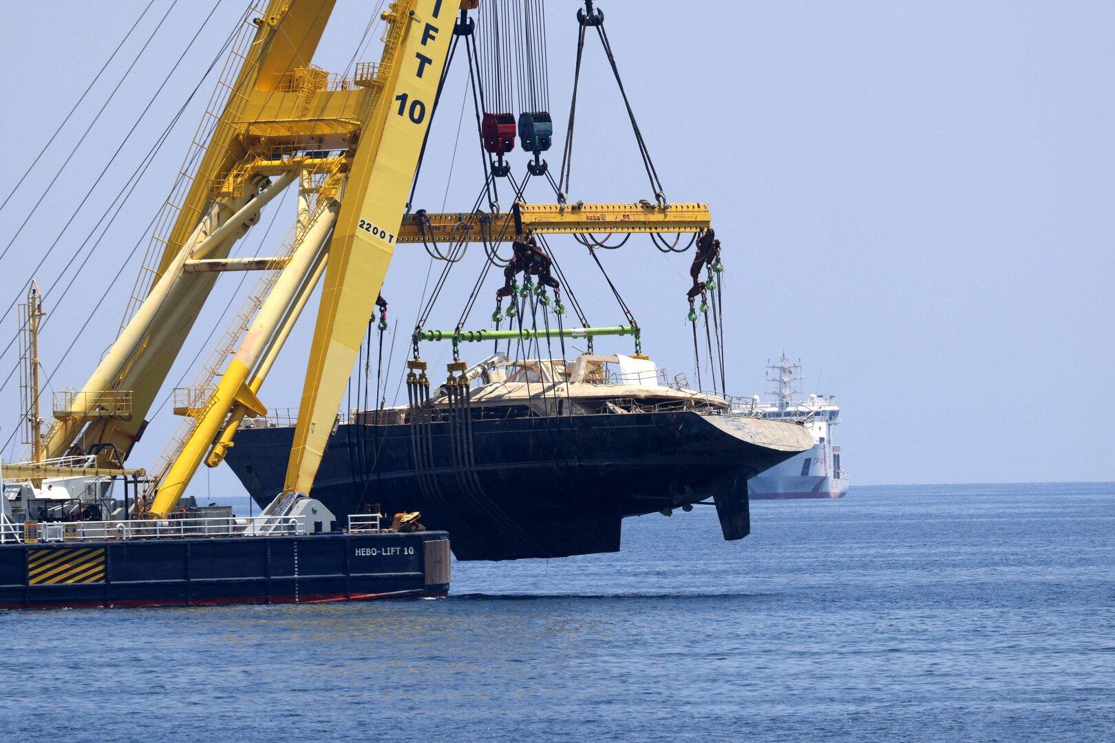 Ein beschädigtes Segelboot wird von einem Kran auf ein Schiff gehoben.