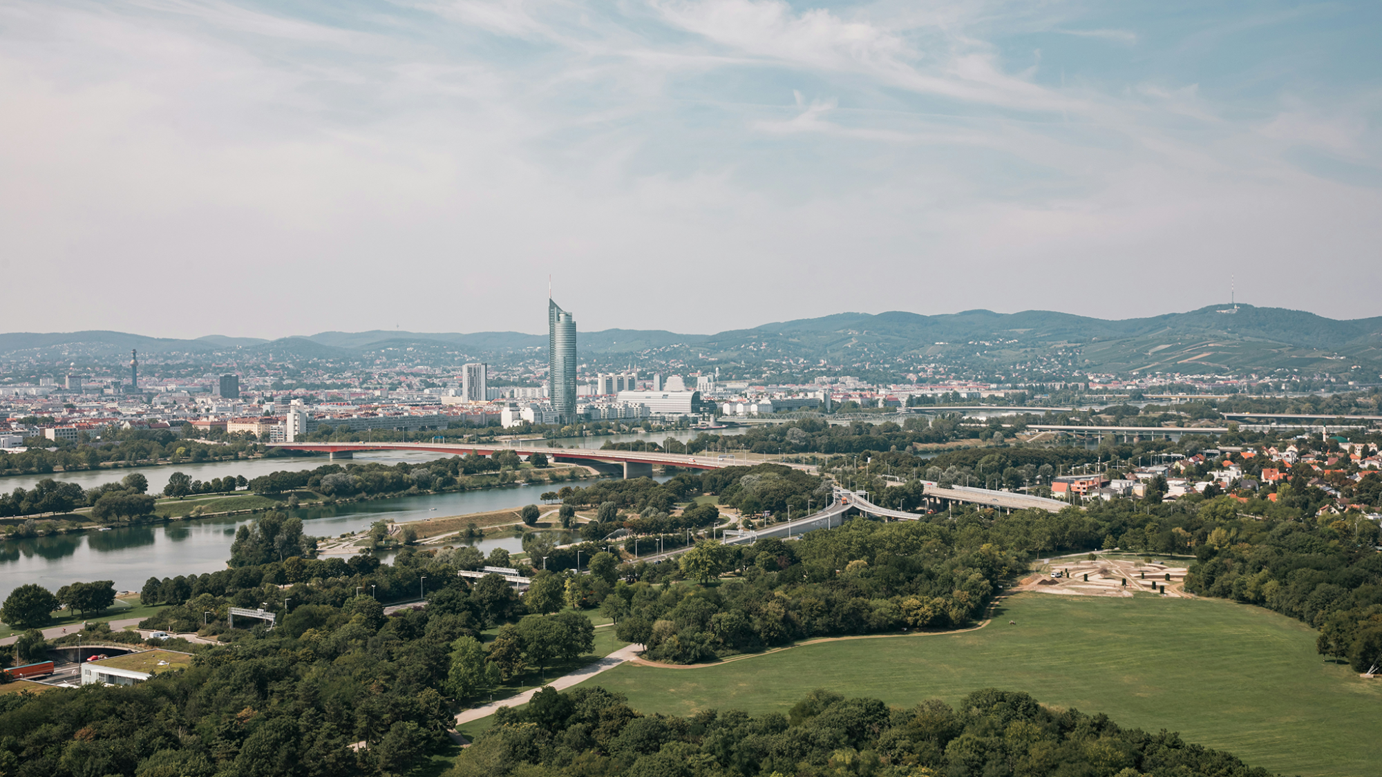 Luftaufnahme der Donaustadt Wien mit Gebäuden, Straßen und Grünflächen, die sich unter einem klaren Himmel erstrecken.