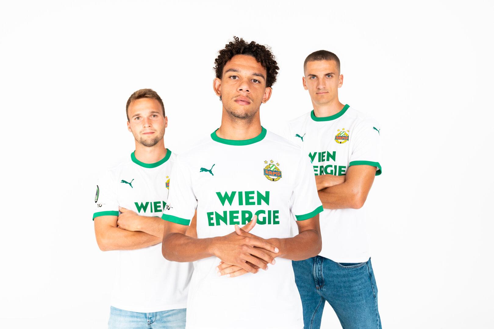 Drei Fußballspieler von Rapid Wien posieren in ihren Trikots.