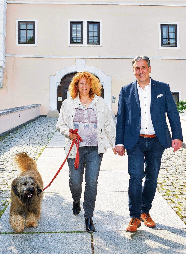 Ein Paar geht mit einem Hund vor einem Gebäude spazieren.