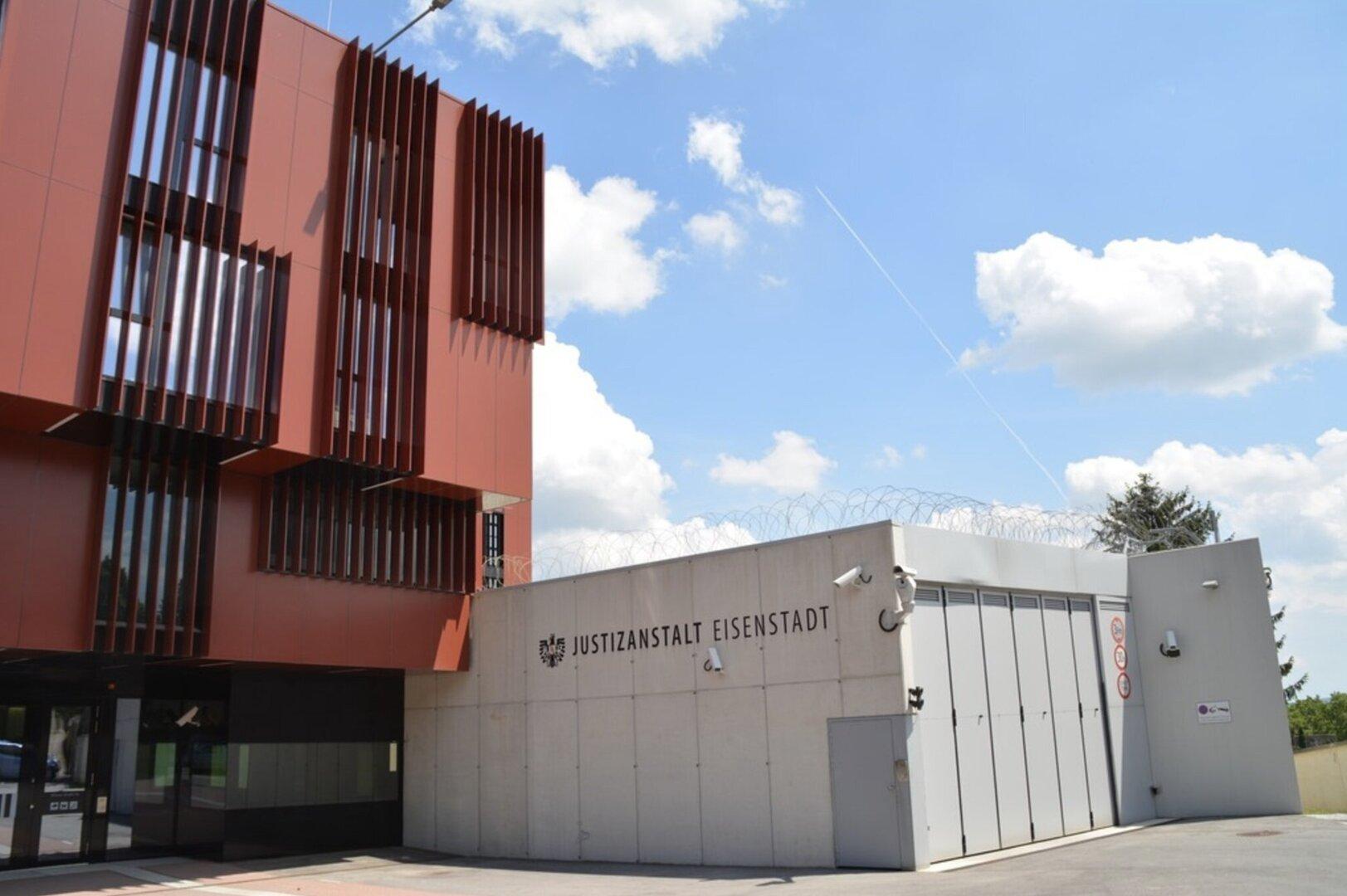 Modernes Gebäude mit roten Fassadenelementen und einem gesicherten Bereich mit Stacheldraht und Überwachungskameras.