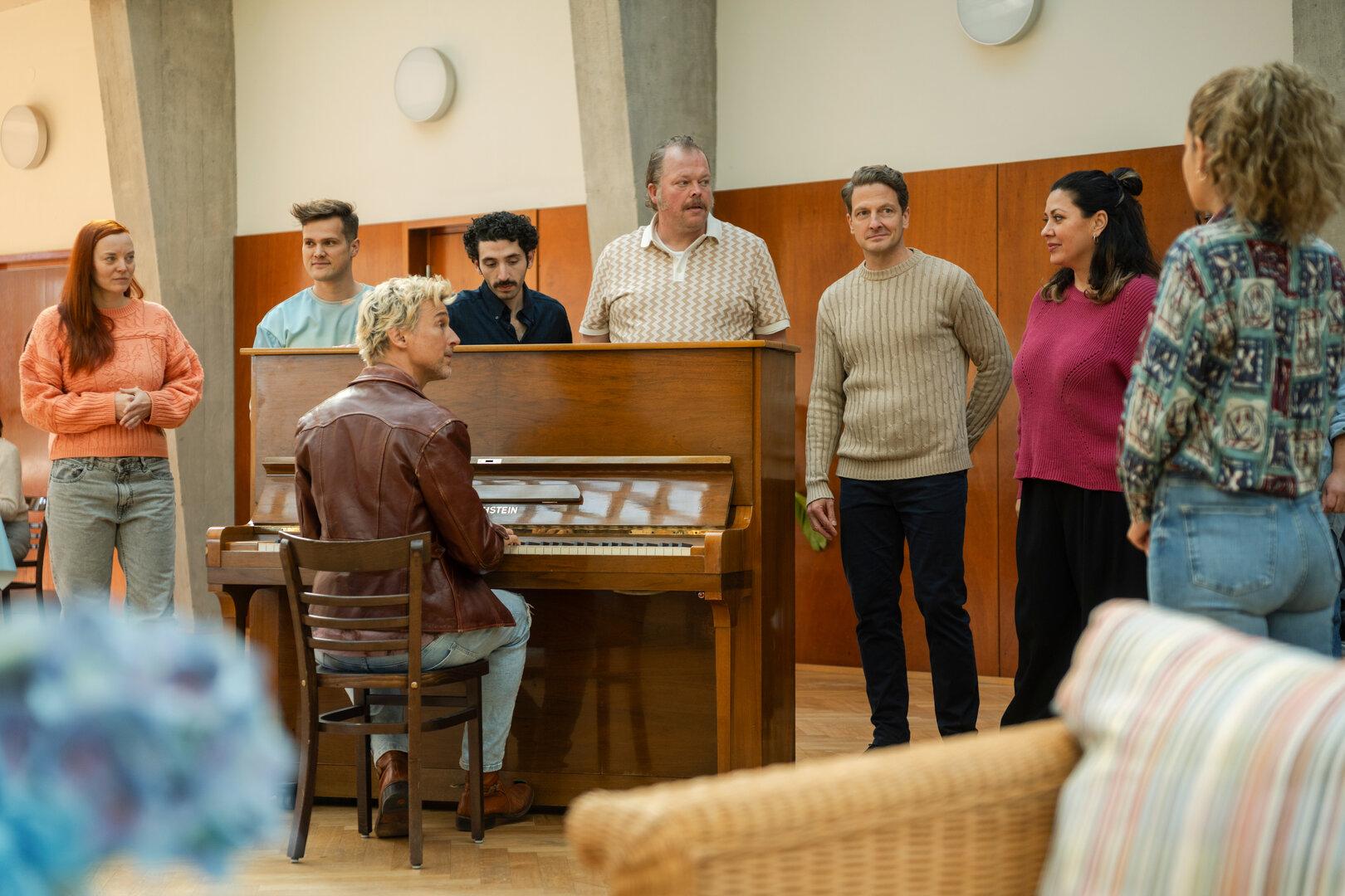 Eine Gruppe von Menschen steht um ein Klavier.