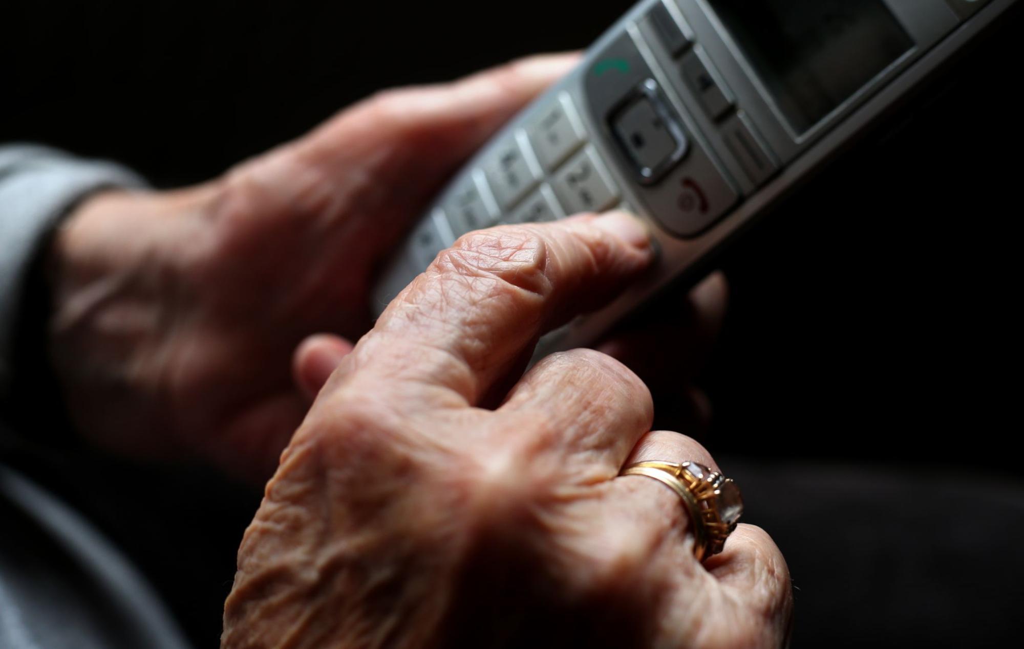 Eine ältere Hand mit Ring tippt auf die Tasten eines schnurlosen Telefons.