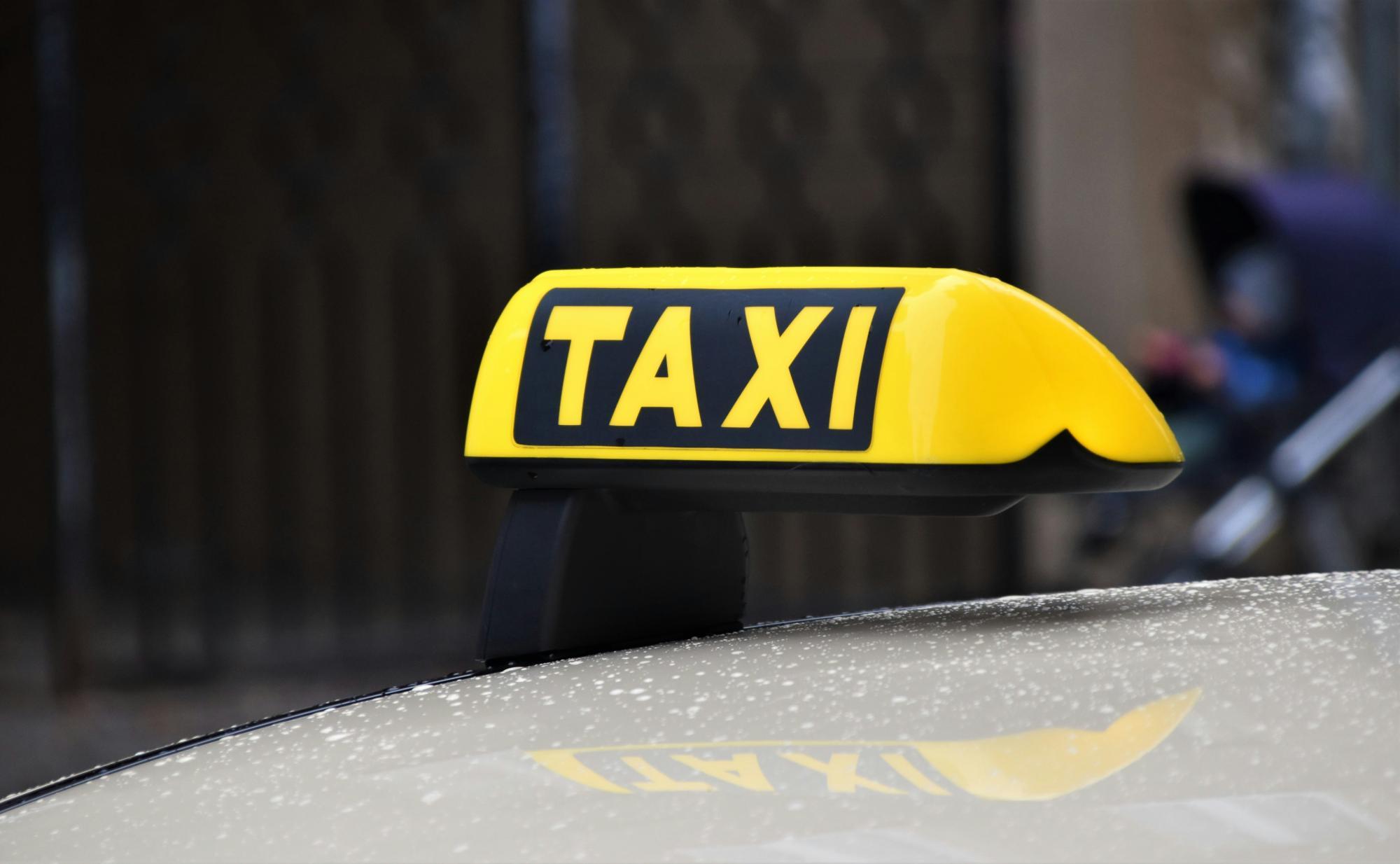 Gelbes TAXI-Dachzeichen auf einem Auto, im Hintergrund unscharf.