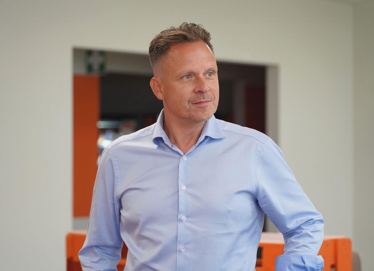 Ein Mann mit kurzem, braunem Haar und hellblauem Hemd blickt zur Seite.