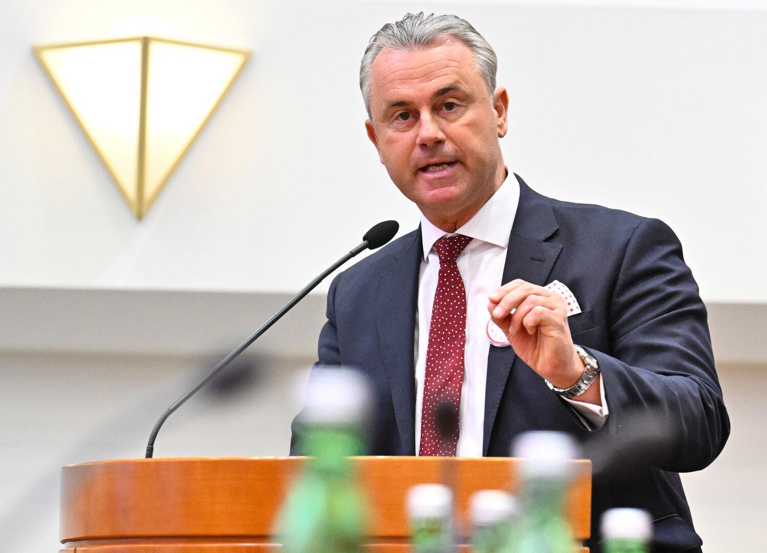 Ein Mann im Anzug spricht an einem Rednerpult mit Mikrofon, im Vordergrund stehen mehrere Flaschen.