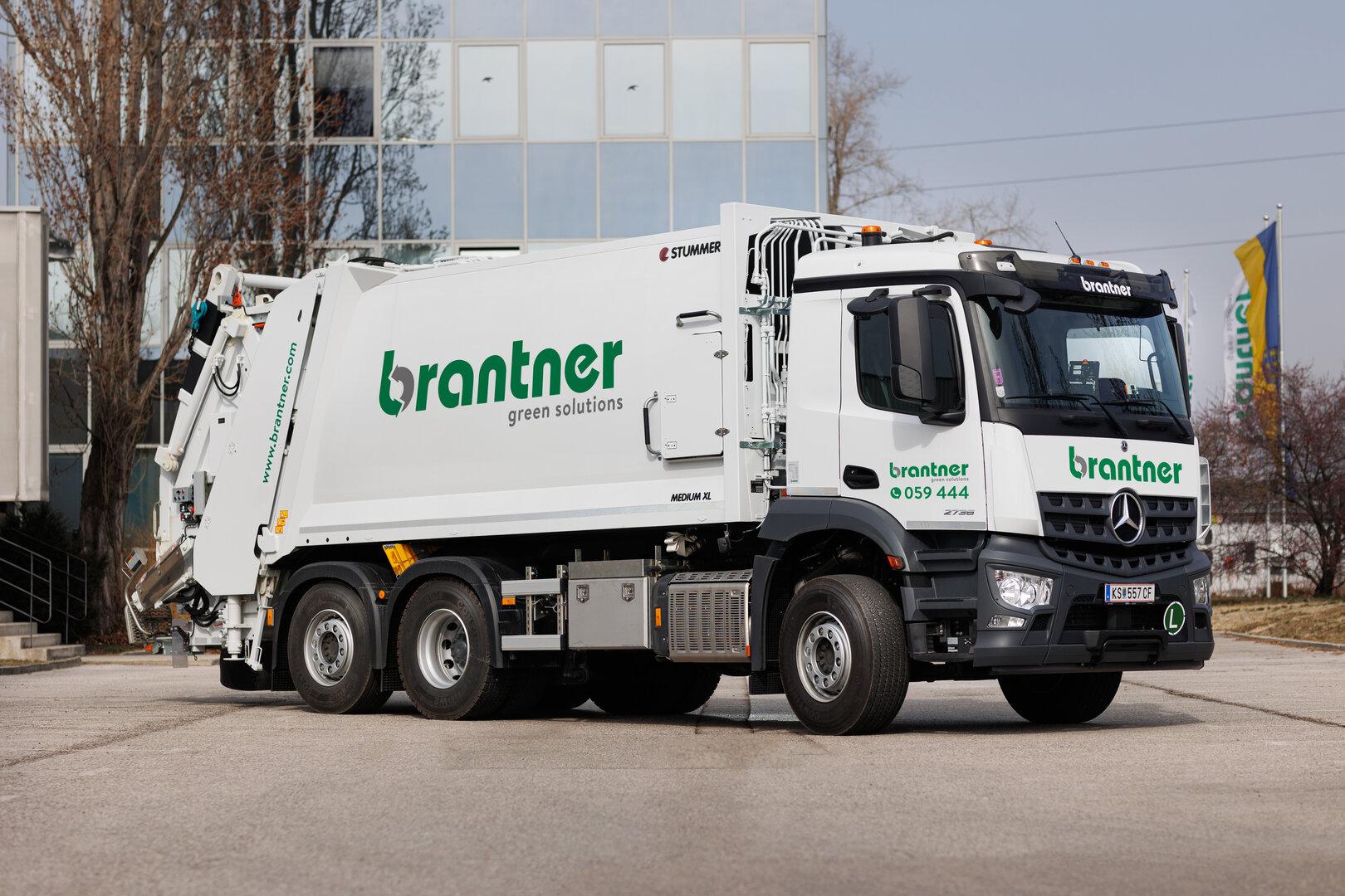 Weißer Müllwagen der Marke Brantner vor einem Gebäude.