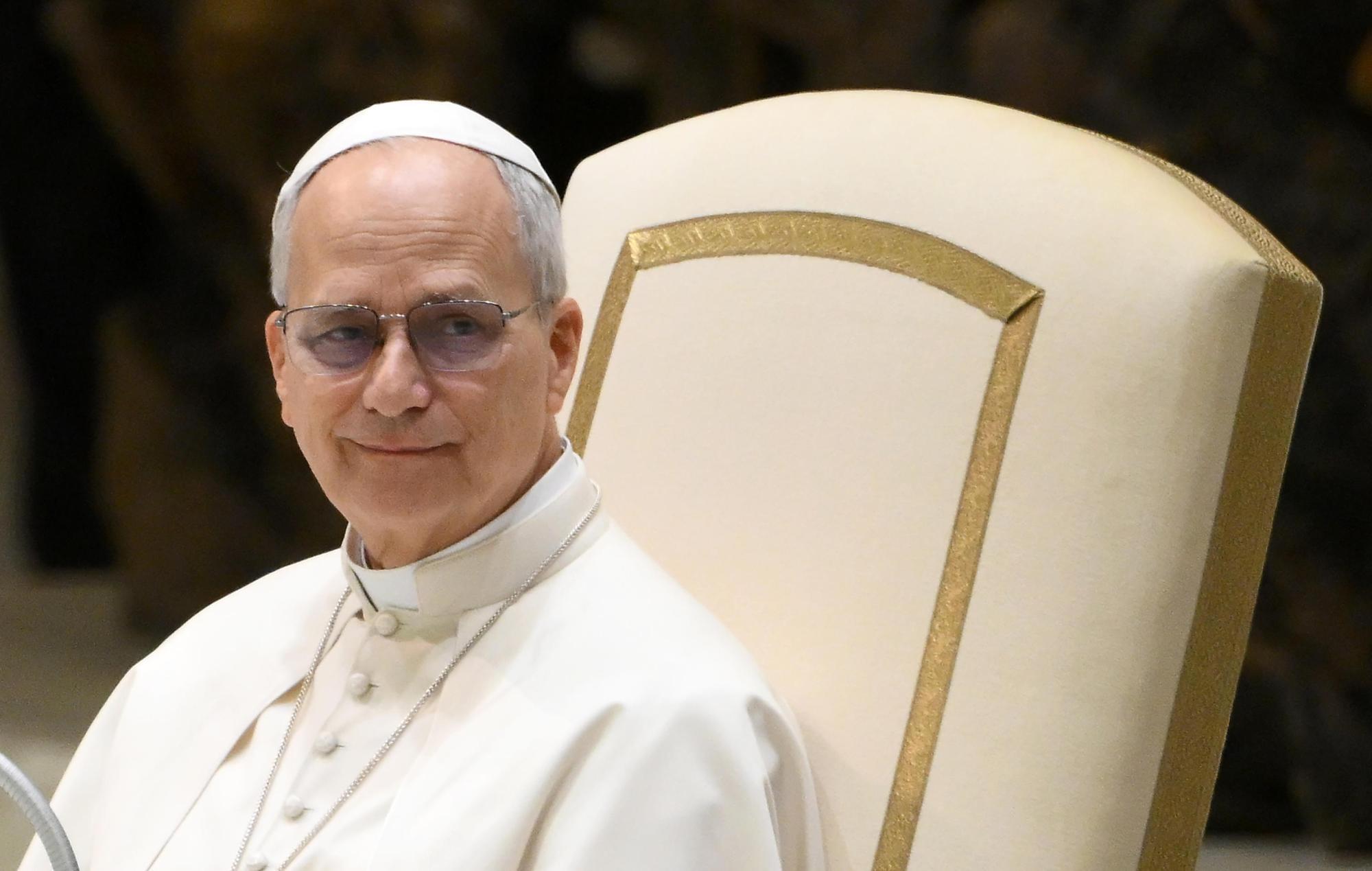 Ein Mann mit Brille und weißem Gewand sitzt auf einem verzierten Stuhl.