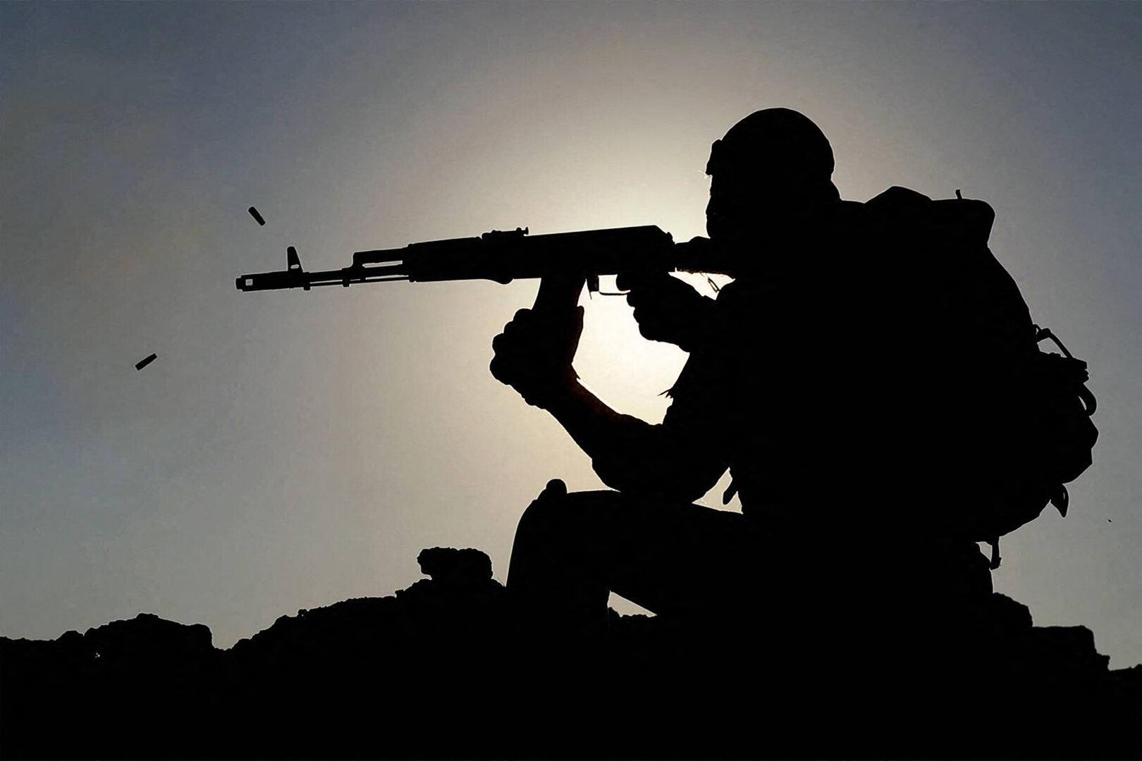 Eine bewaffnete Person in Schutzausrüstung schießt im Gegenlicht, Patronenhülsen fliegen durch die Luft.