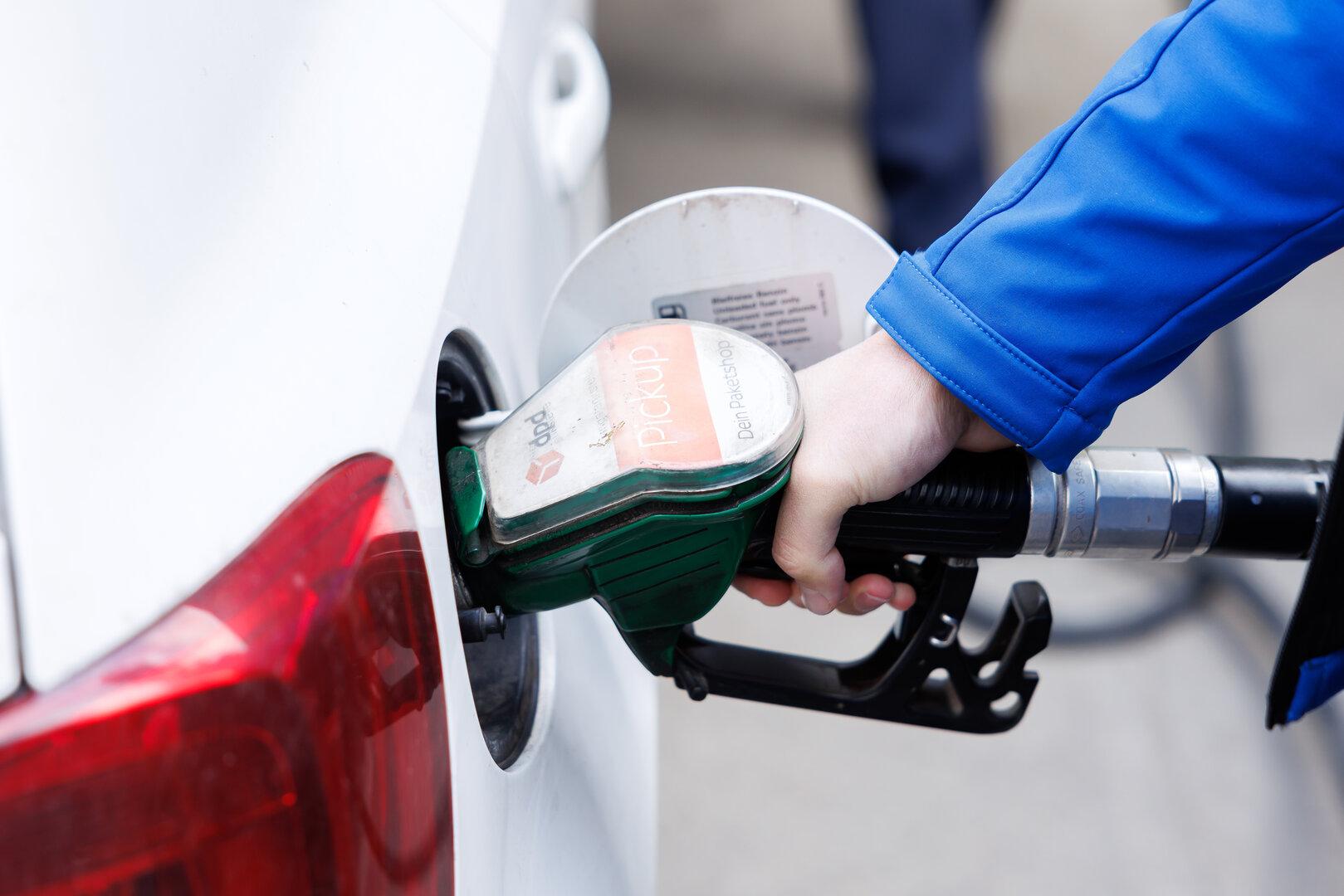 Eine Person tankt ein weißes Auto mit einer grünen Zapfpistole an einer Tankstelle.