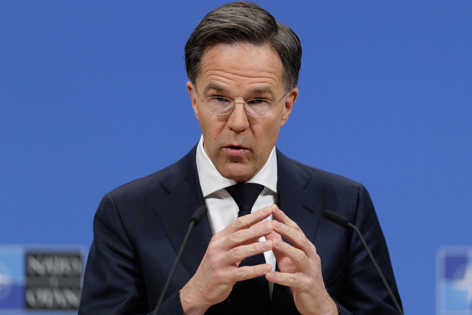 Mark Rutte spricht vor einem blauen Hintergrund und gestikuliert mit den Händen.