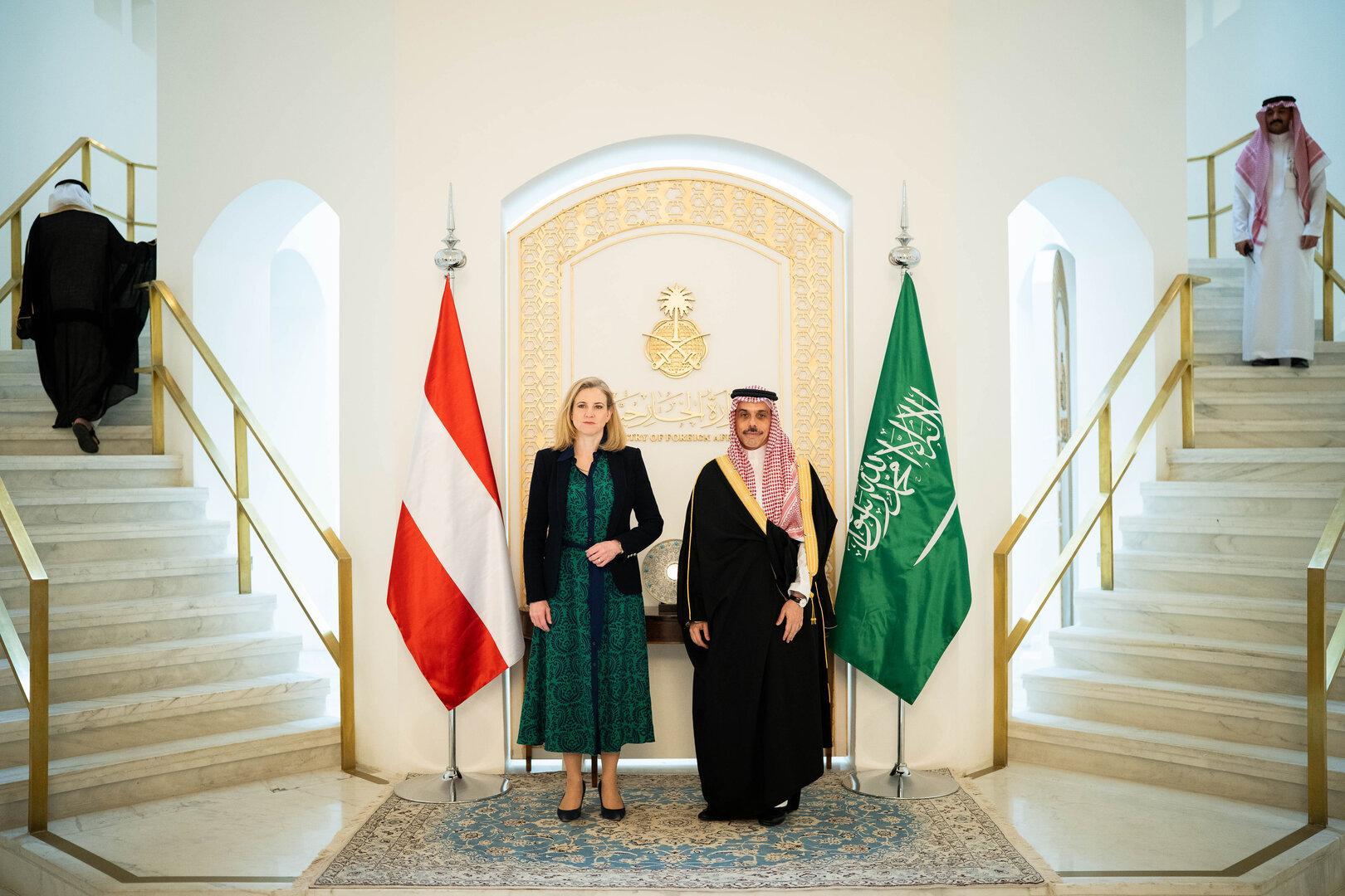 Zwei Personen stehen zwischen der österreichischen und der saudi-arabischen Flagge in einem repräsentativen Gebäude.