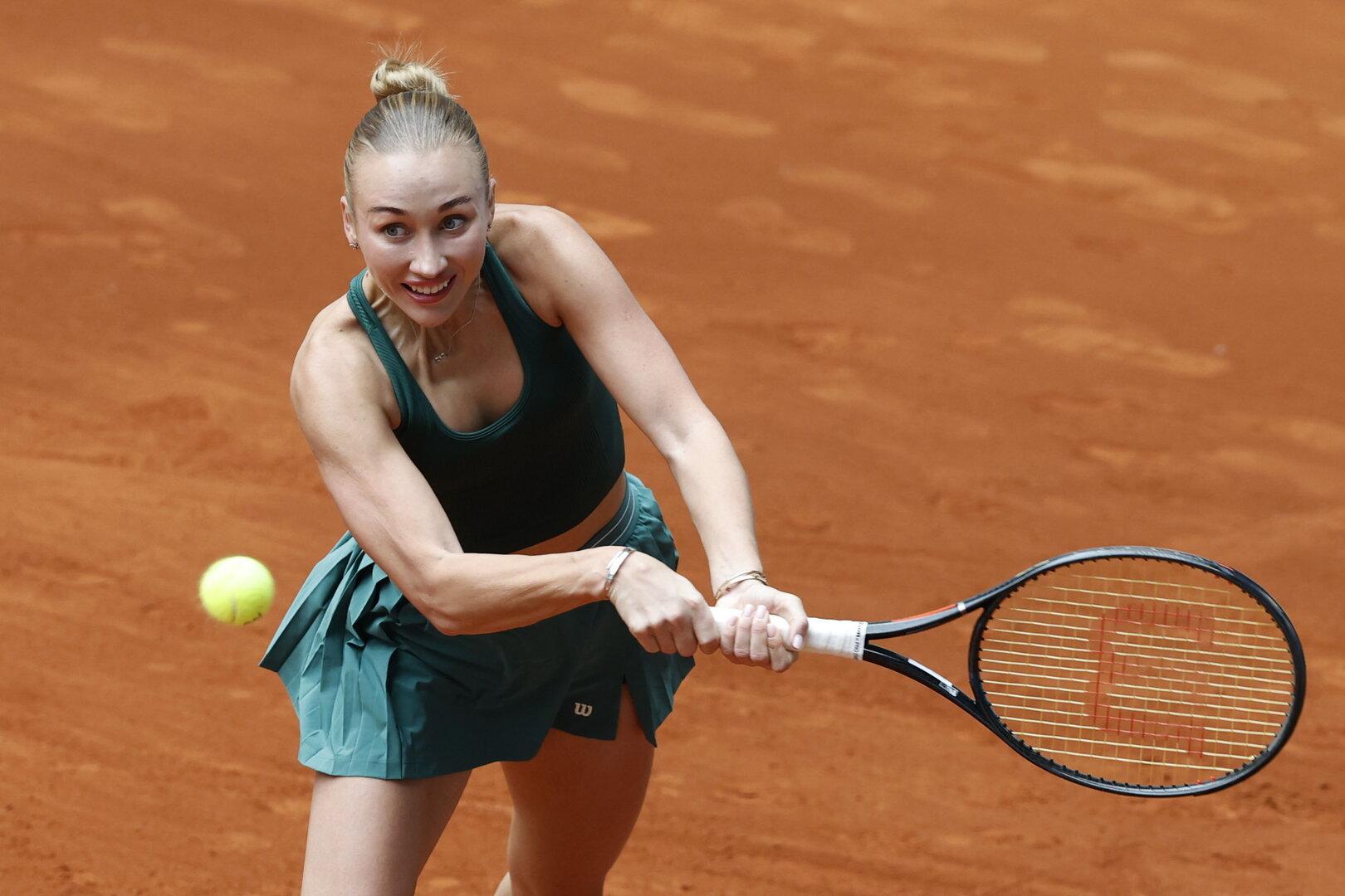 Eine Tennisspielerin in grüner Sportkleidung schlägt einen Ball mit ihrem Schläger.