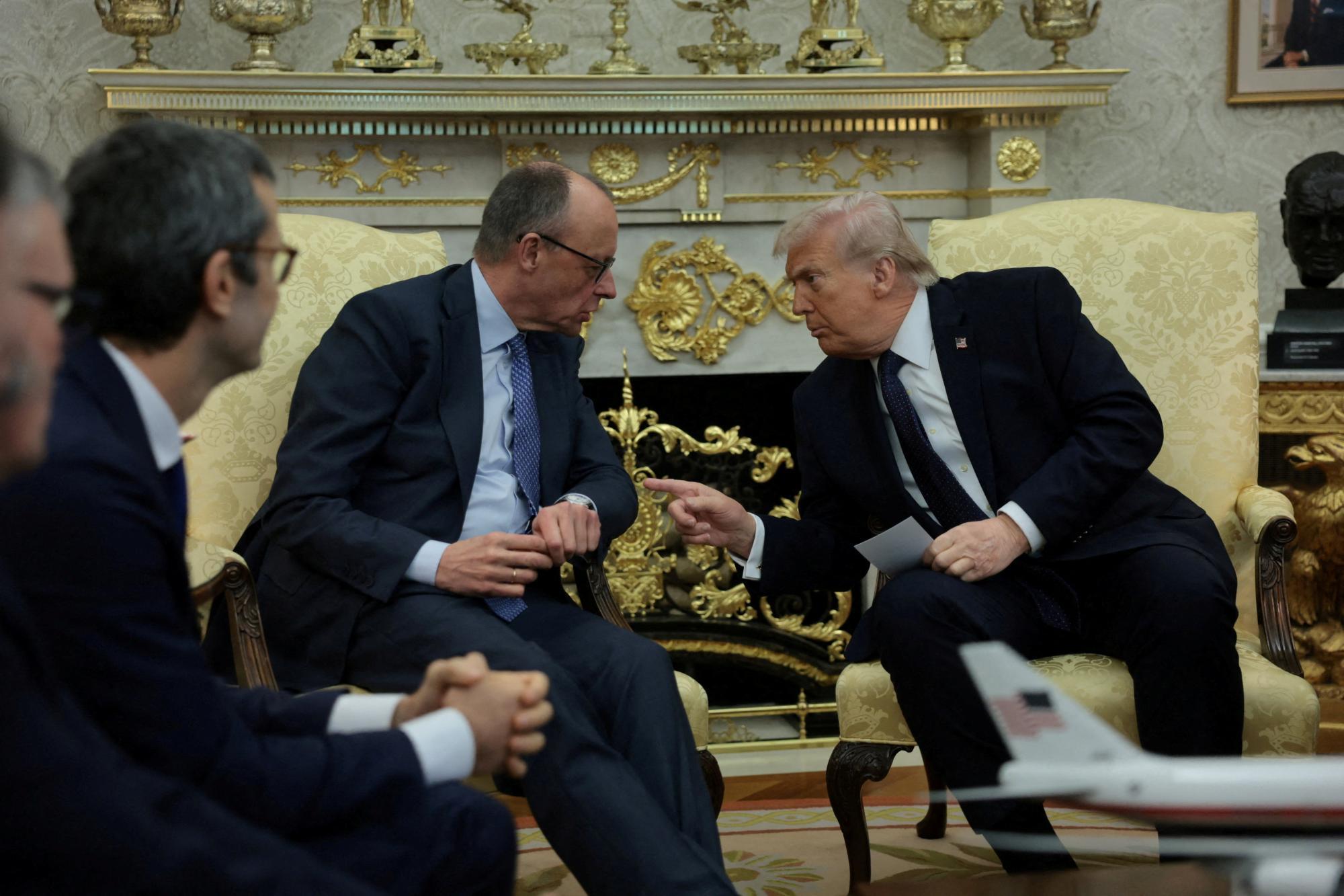 Donald Trump gestikuliert während eines Gesprächs mit einem Mann im Anzug in einem dekorierten Raum.