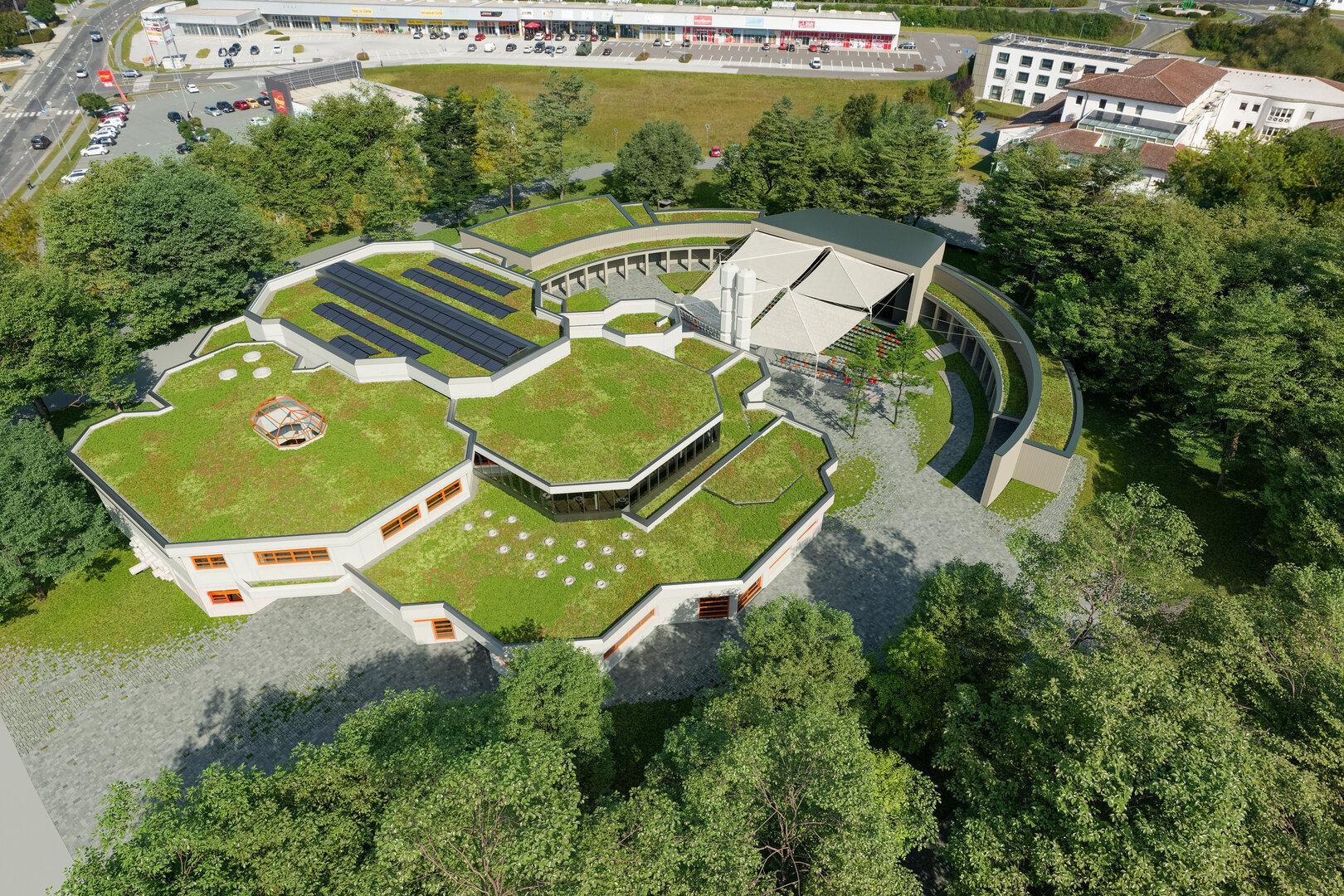 Gebäude mit begrüntem Dach, Solarpaneelen und moderner, geometrischer Architektur, umgeben von Bäumen und Parkplätzen.