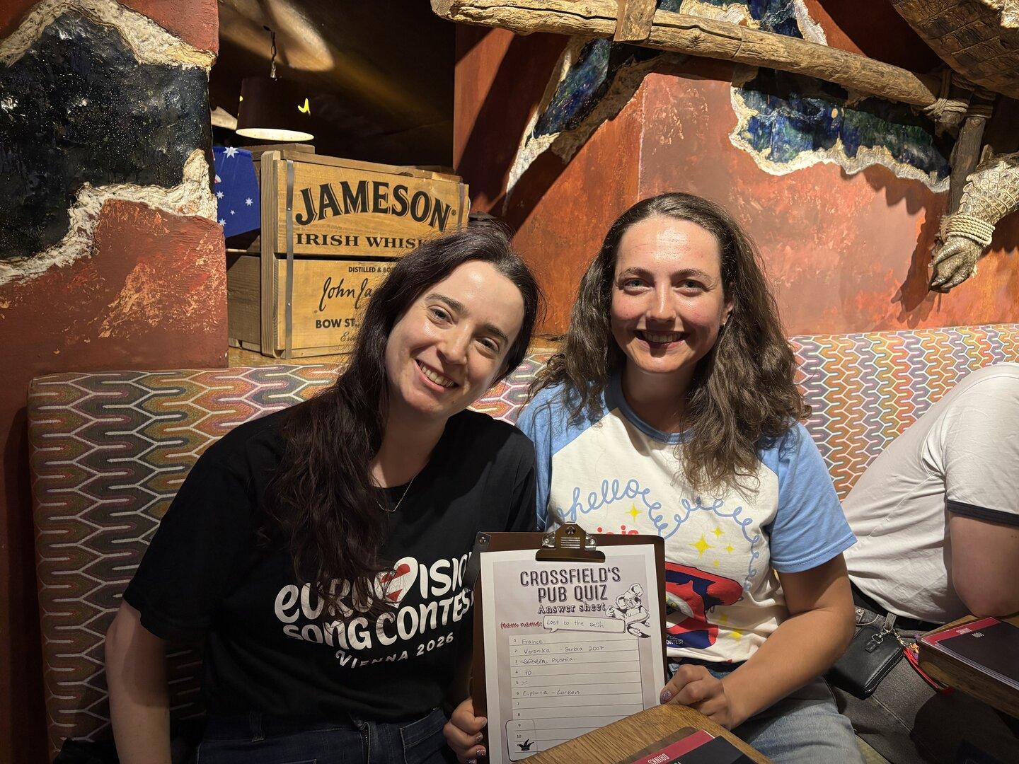 Zwei Frauen lächeln mit einem "Crossfield's Pub Quiz"-Bogen und einem "Eurovision Song Contest"-T-Shirt.