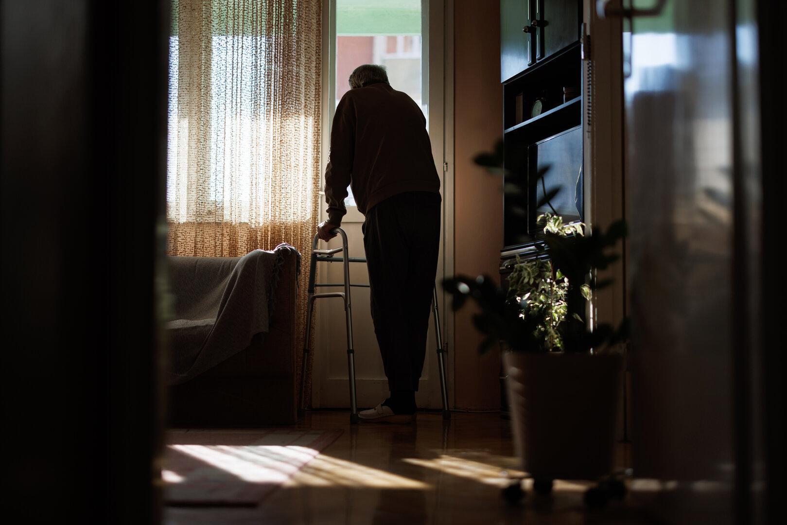 Elderly man with walker looking out window, contemplating life in quiet solitude