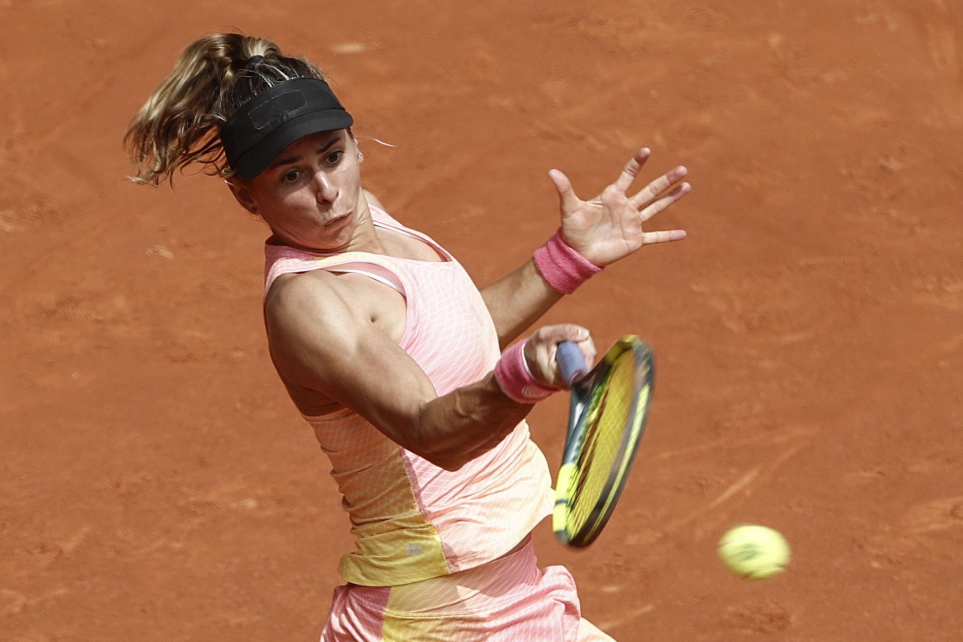 Eine Tennisspielerin mit Schirmmütze schlägt einen Ball auf einem Sandplatz.