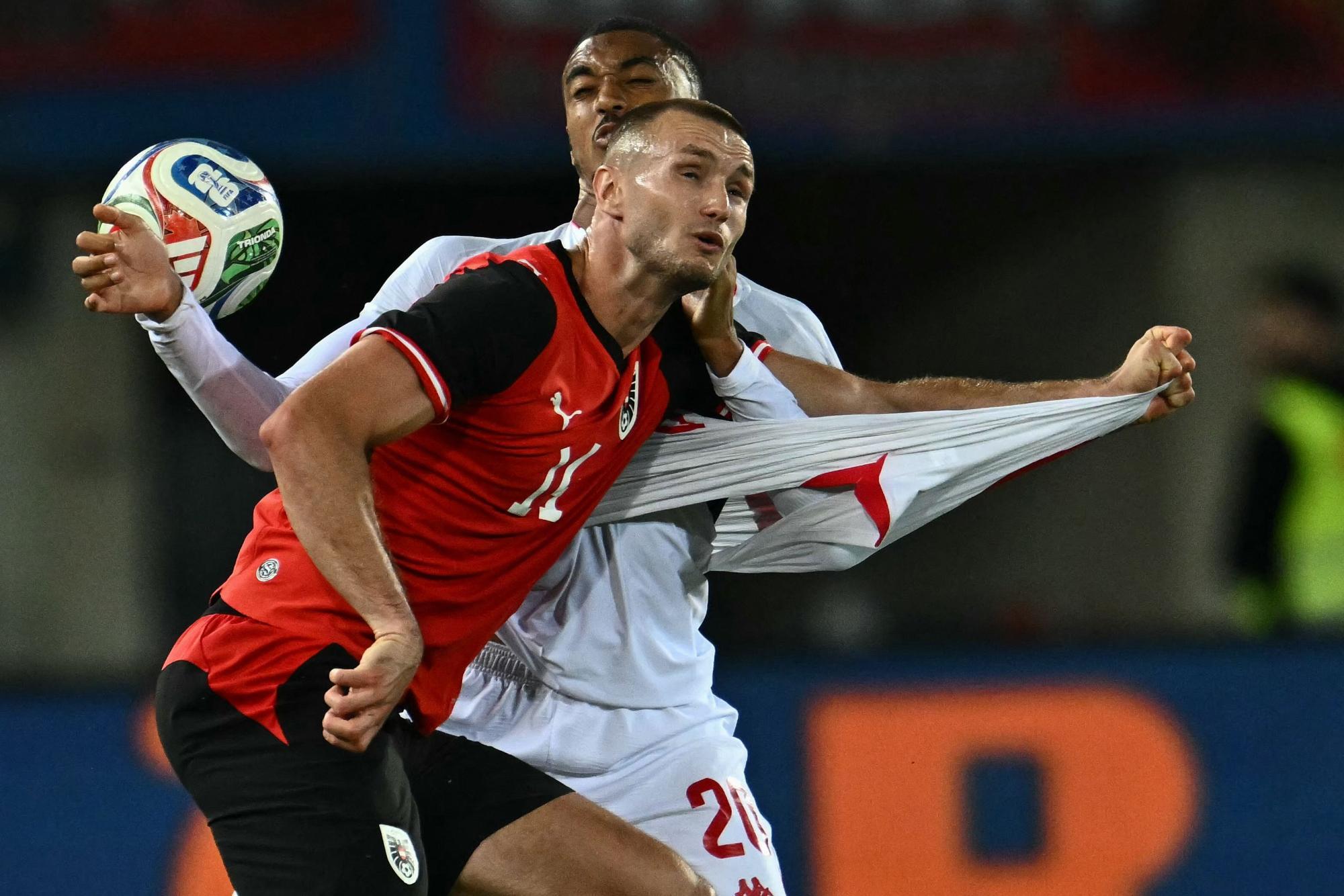 Zwei Fußballspieler kämpfen um den Ball, einer zieht am Trikot des anderen.