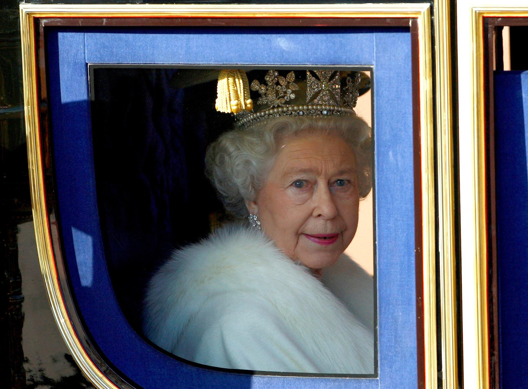 Queen Elizabeth mit einer Krone auf dem Kopf blickt durch das Fenster einer Kutsche