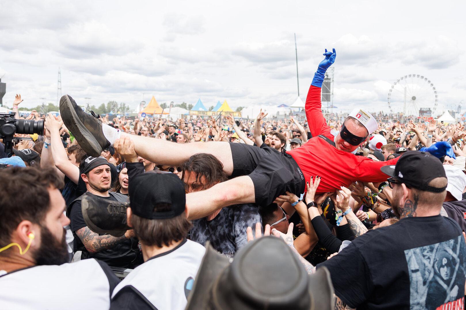 Eine verkleidete Person wird beim Crowdsurfing von einer großen, feiernden Menschenmenge getragen.