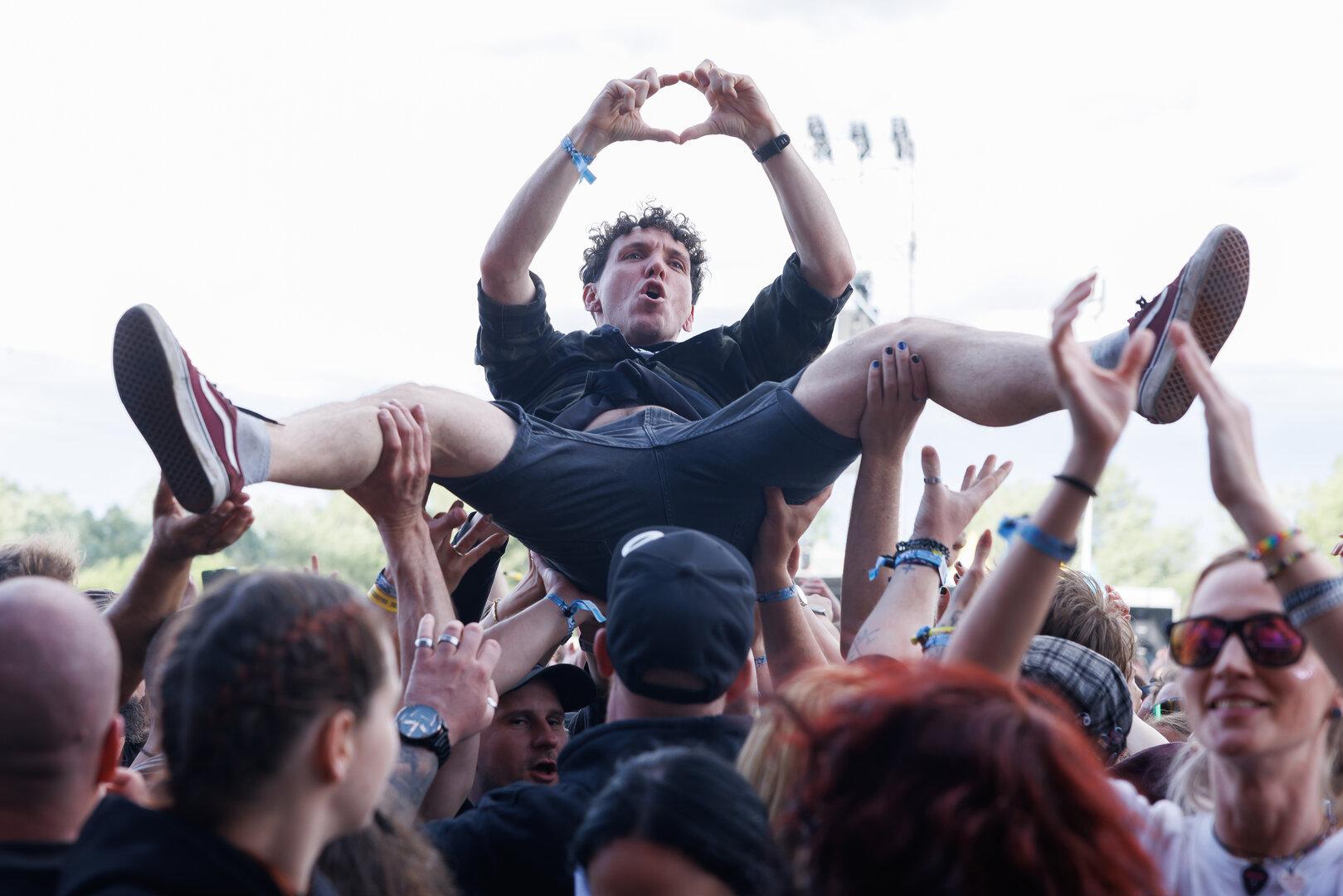 Eine Menschenmenge trägt eine Person beim Crowdsurfing, die mit den Händen ein Herz formt.