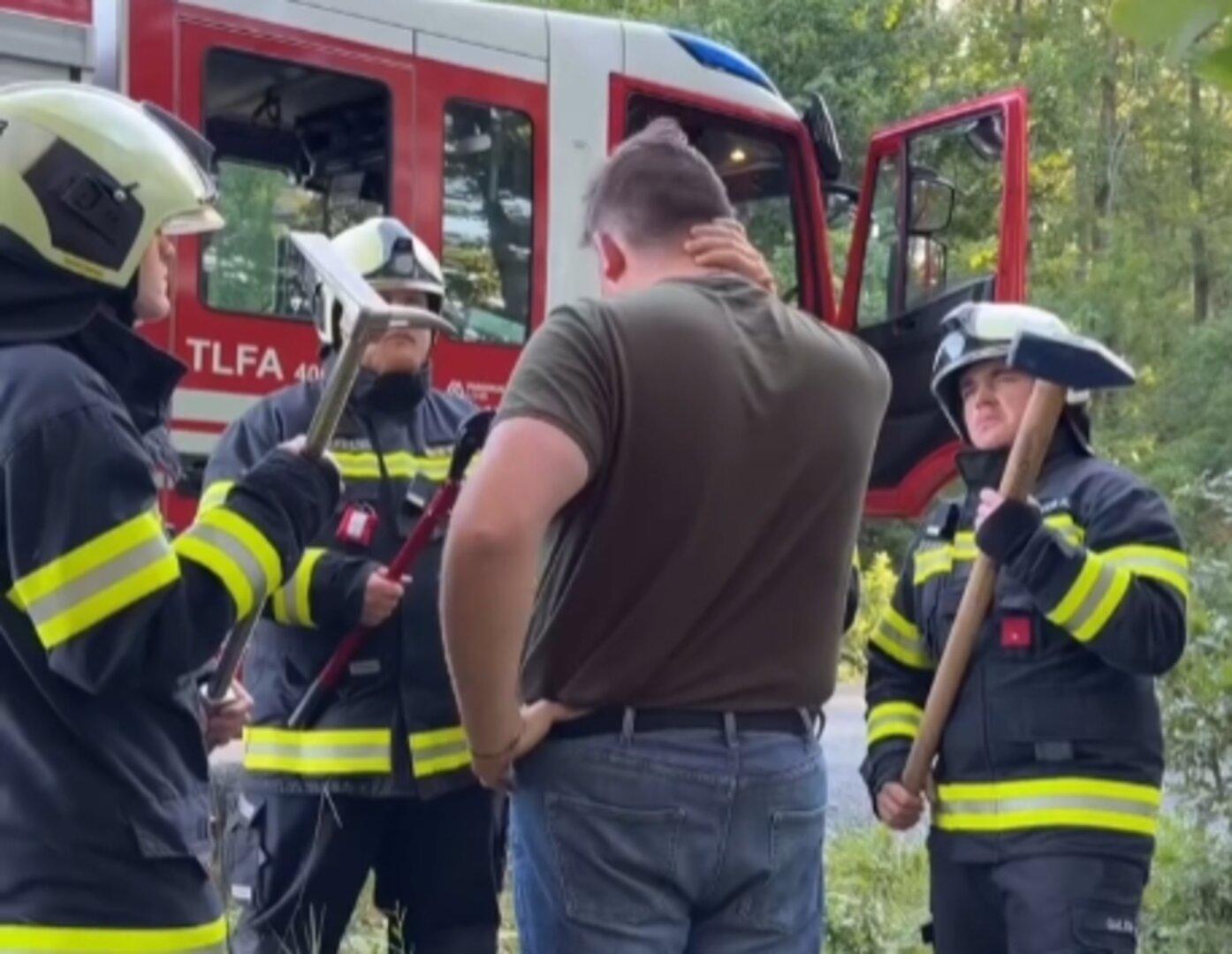 Drei Feuerwehrleute in Uniform sprechen mit einem Mann vor einem Einsatzfahrzeug im Grünen.