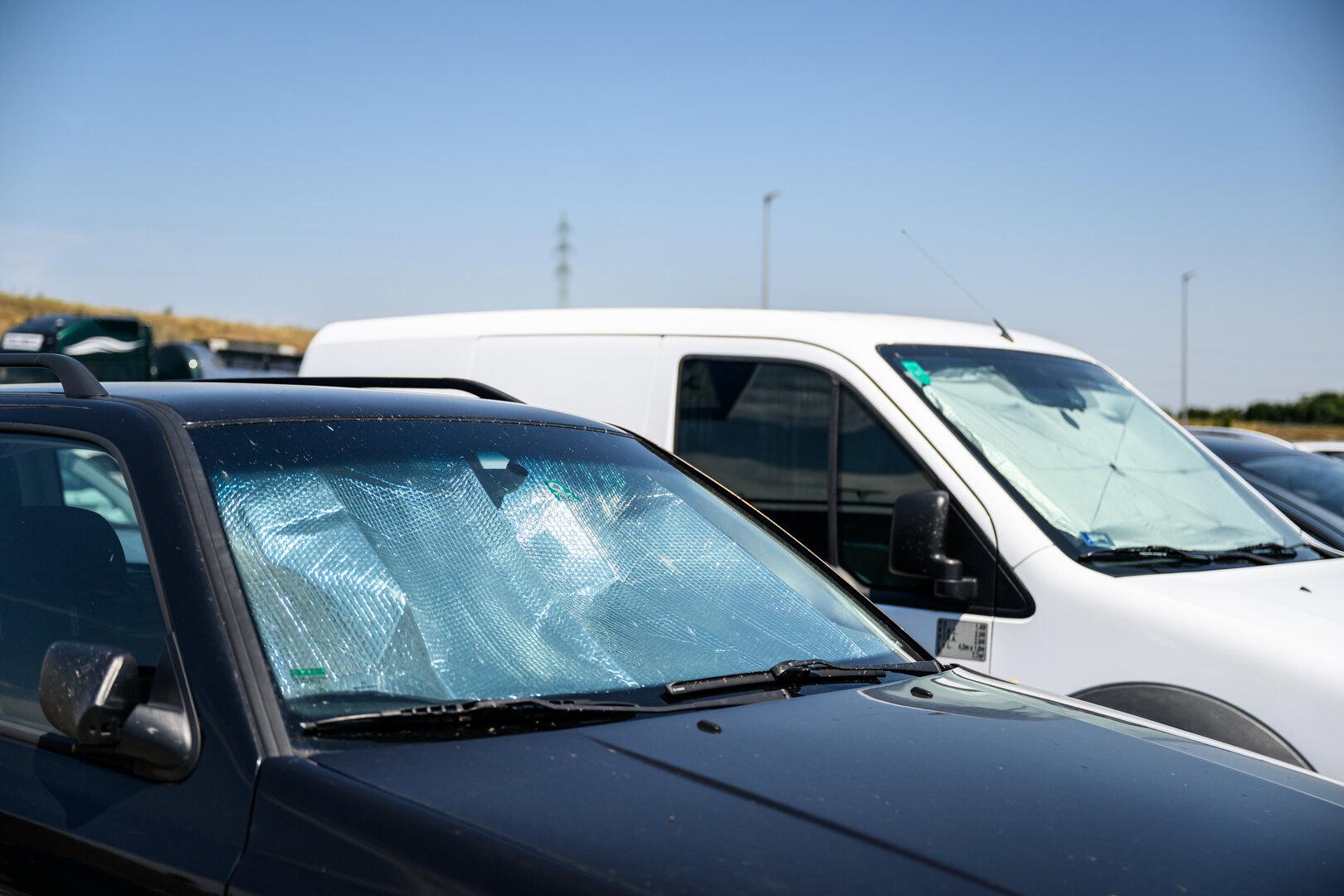 Mehrere geparkte Transporter und Autos mit Sonnenschutz an den Frontscheiben auf einem Parkplatz.