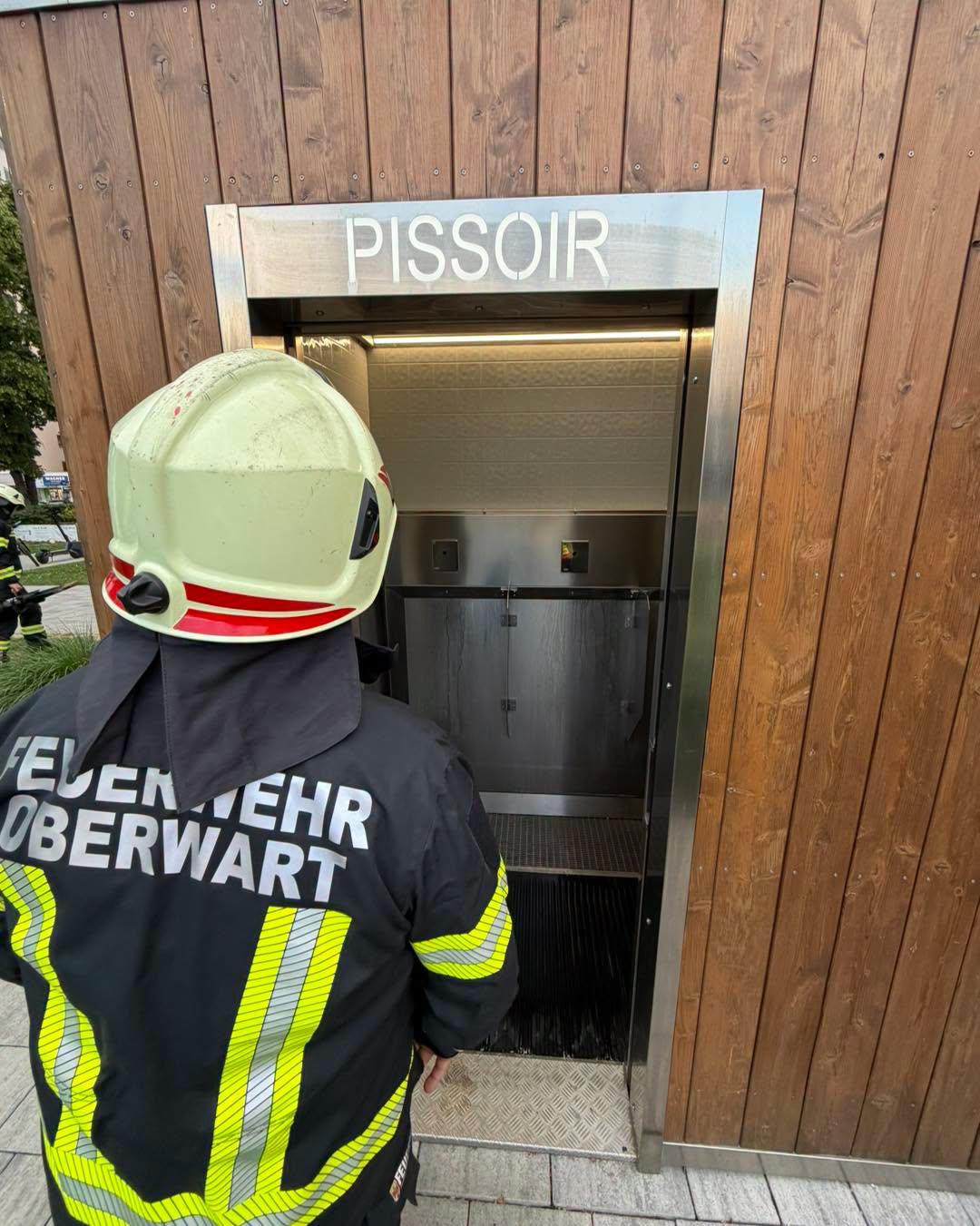 Feuerwehrmann vor öffentlicher Toilettenanlage mit offener Tür.
