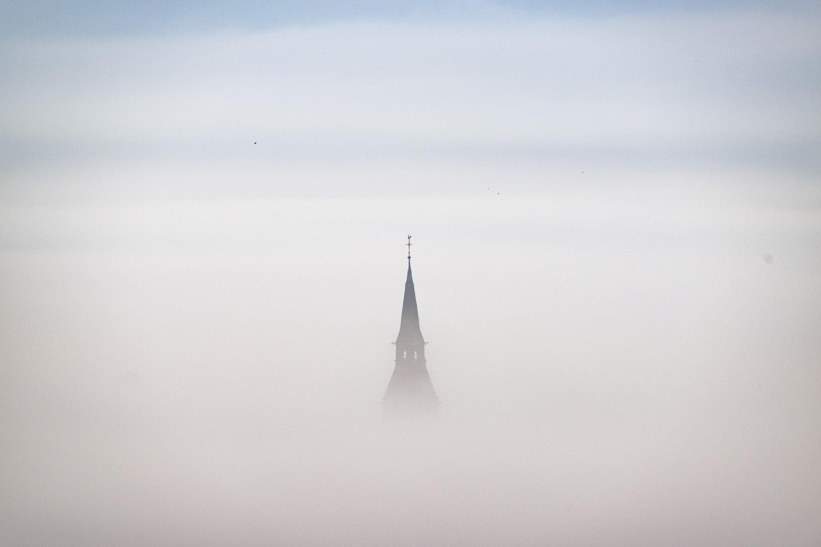 Kirchturmspitze ragt aus dichtem Nebel empor.