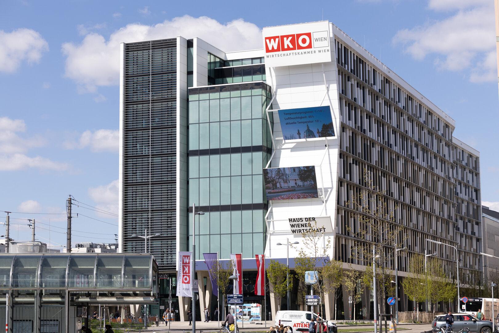 Das moderne Gebäude der WKO Wien mit Glasfassade und digitalen Anzeigetafeln steht unter blauem Himmel.