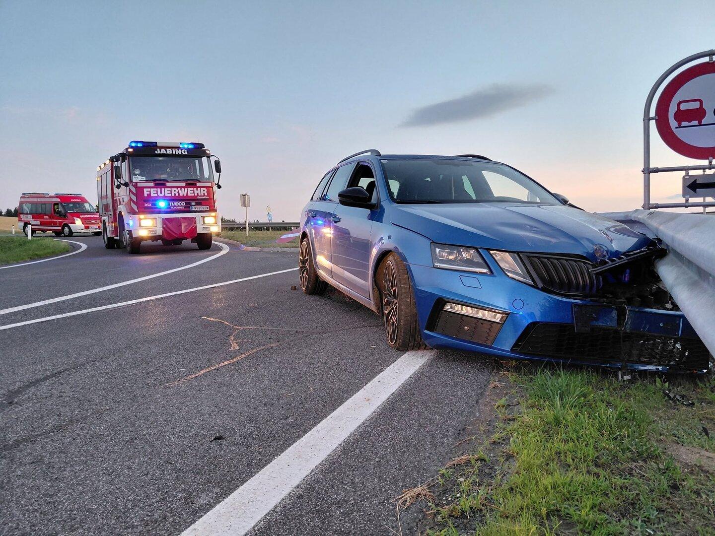 Blauer Kombi ist in die Leitplanke geprallt, Feuerwehrfahrzeuge sichern die Unfallstelle.