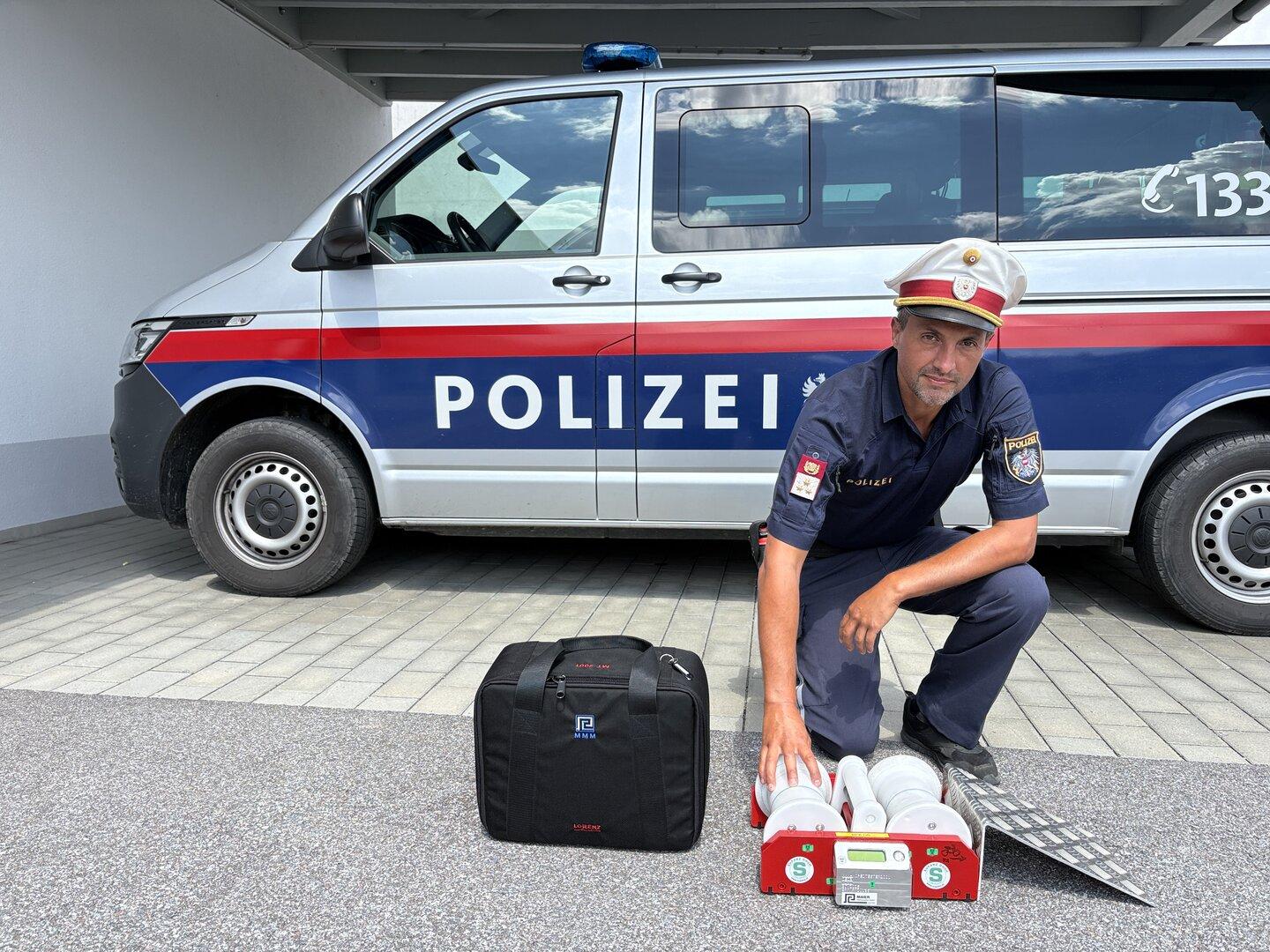 Polizist kniet vor einem Polizeiwagen neben Einsatzgerät und Tasche.
