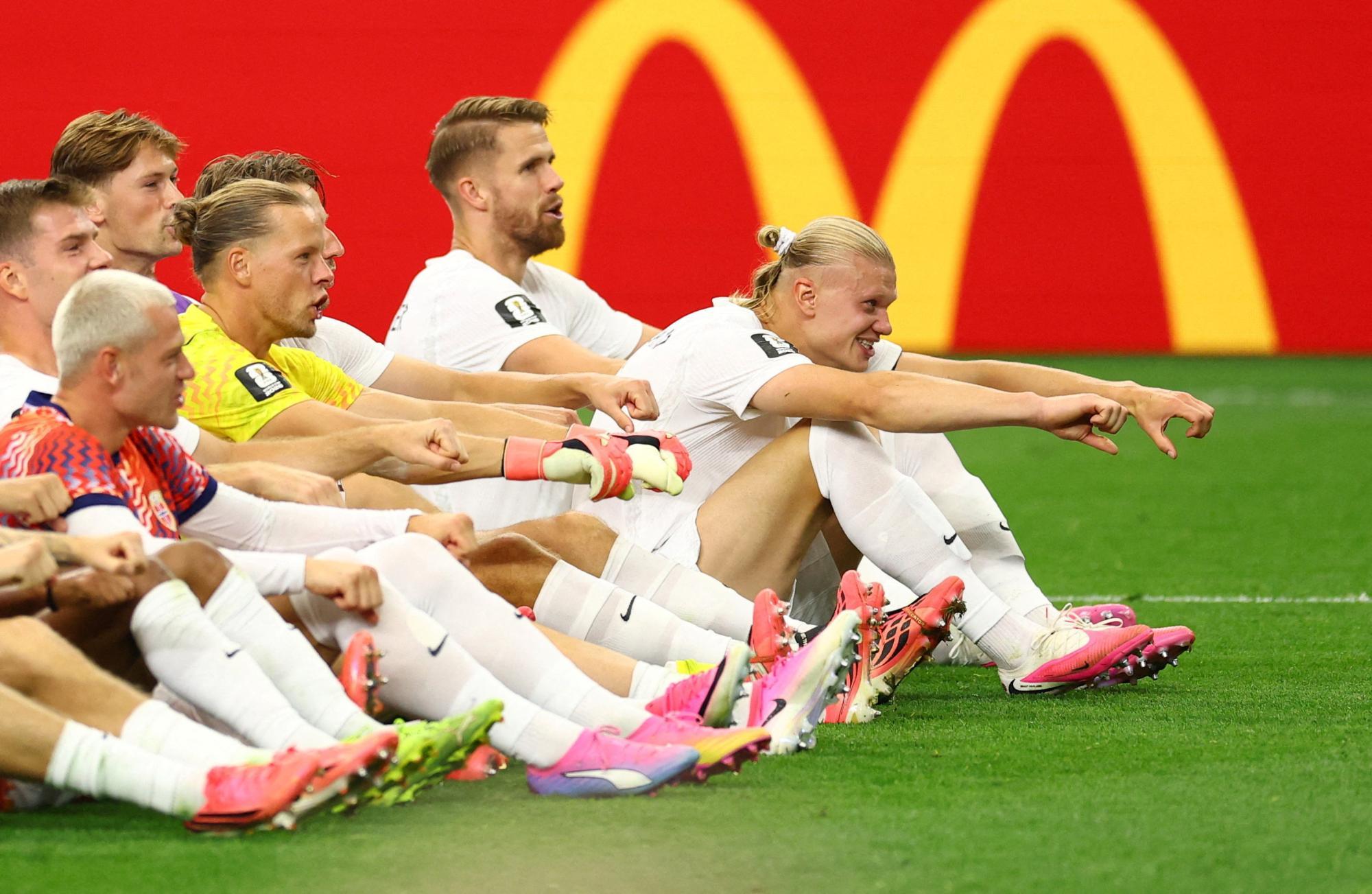 Die norwegische Nationalmannschaft jubelt sitzend auf dem Rasen. Stürmer Erling Haaland streckt seine beiden Arme aus. 