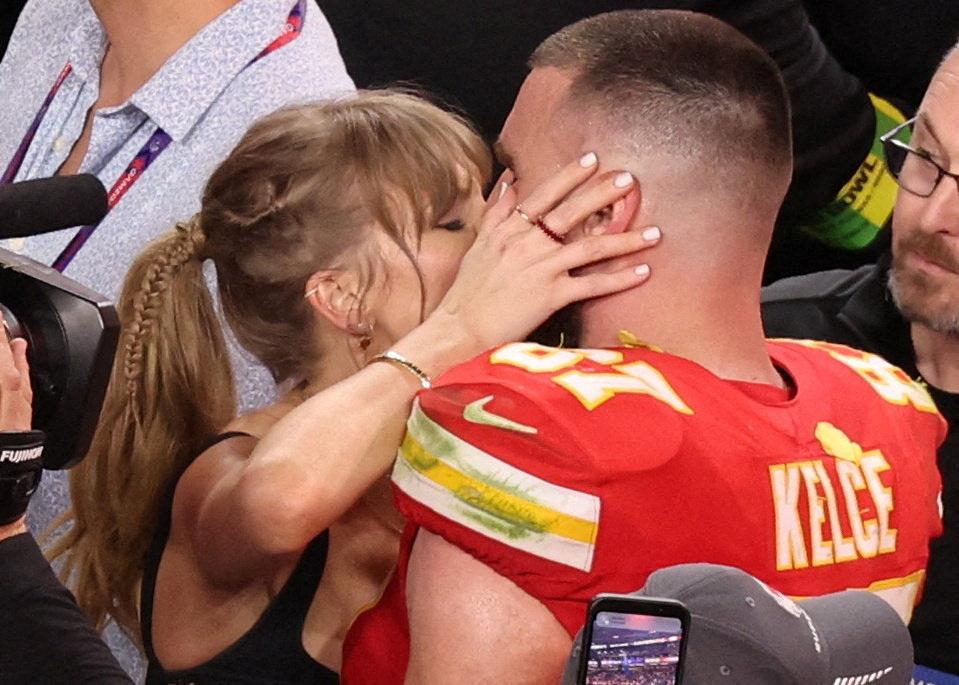 Taylor Swift küsst den Footballspieler Travis Kelce, der ein rotes Trikot der Kansas City Chiefs trägt.