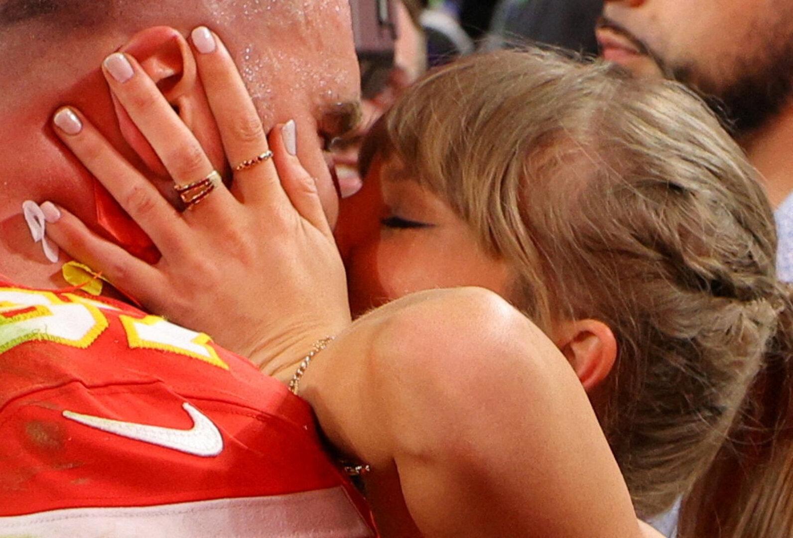 Taylor Swift küsst Travis Kelce, der ein rotes Trikot der Kansas City Chiefs trägt.