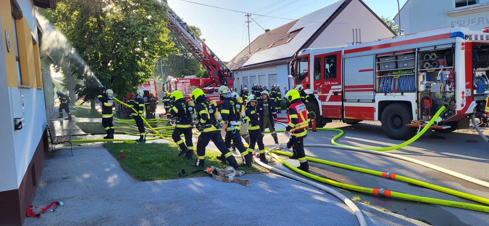 Feuerwehrleute bekämpfen einen Brand mit Schlauchleitungen und Drehleiter vor einem Haus.