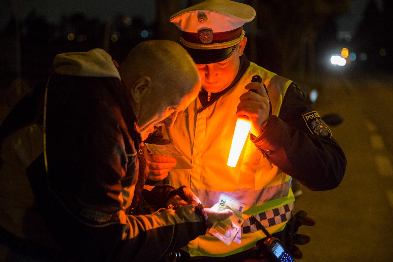 Polizist kontrolliert nachts einen Mann und beleuchtet Geldscheine mit einer Leuchte.