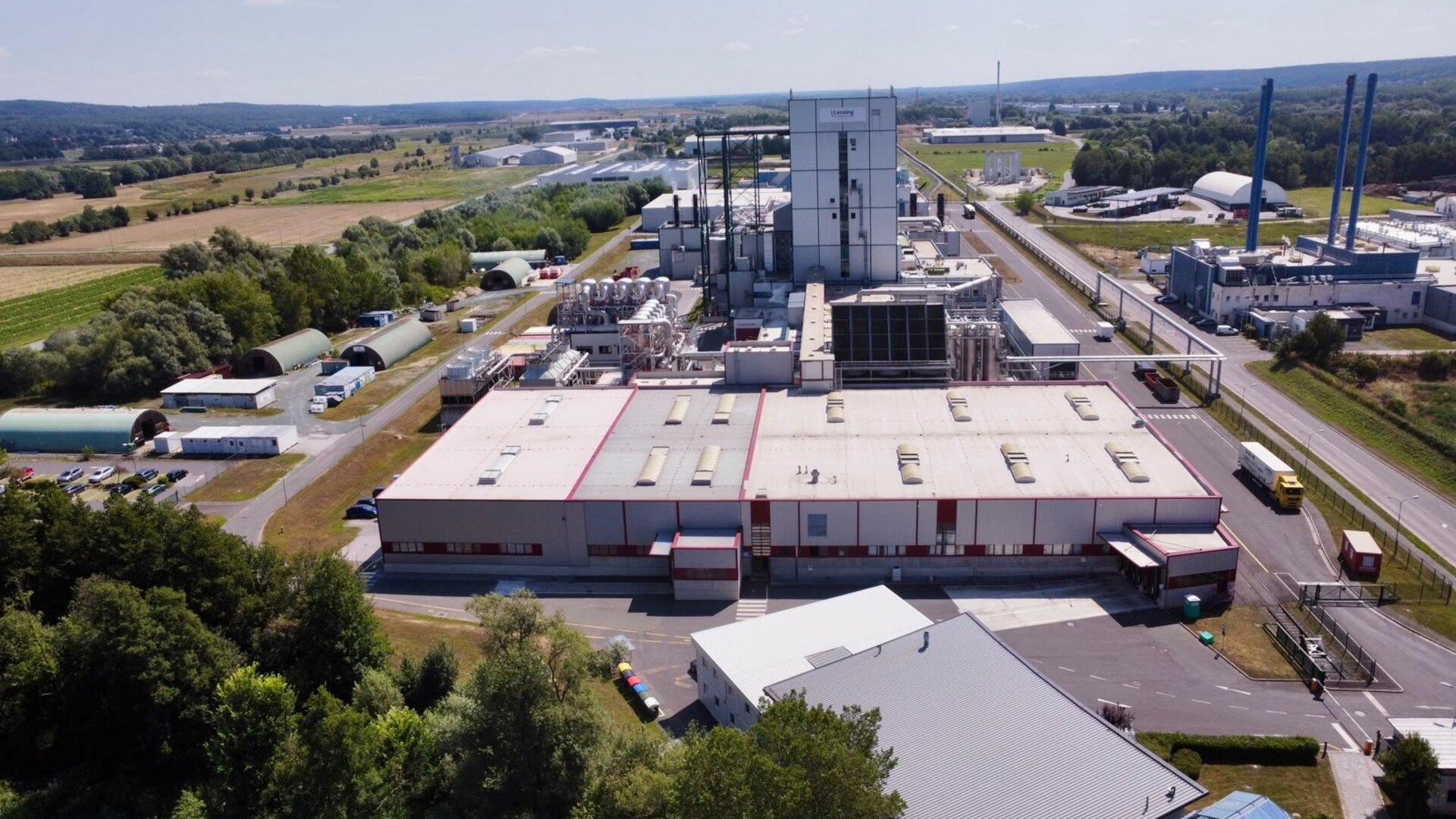 Große Industrieanlage mit Fabrikhallen, Schornsteinen und Straßen in ländlicher Umgebung.