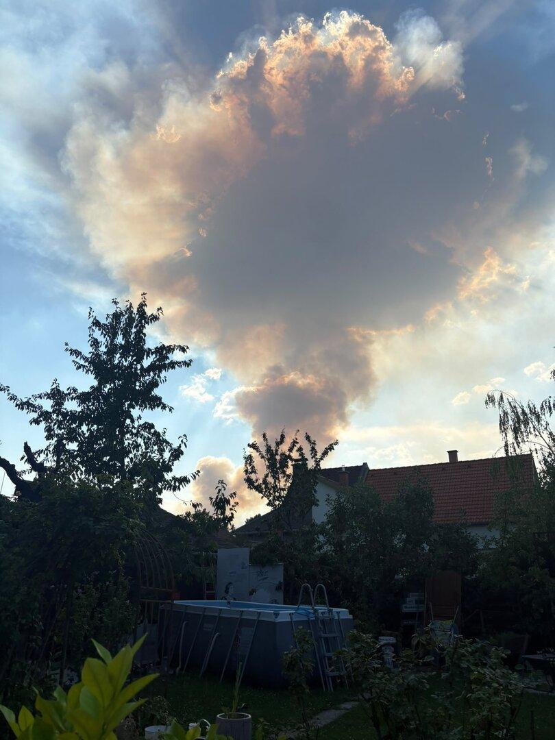 Große, von der Sonne goldgeränderte Wolke über einem Garten mit Pool und Hausdächern.